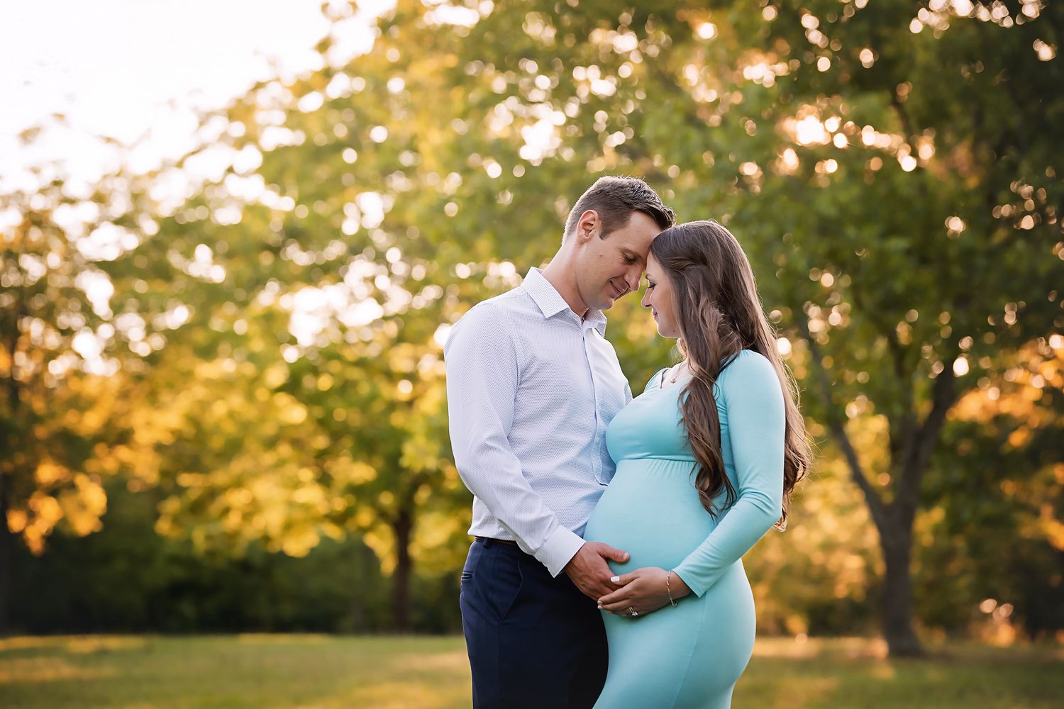 Stunning Lexington SC Maternity Portrait showing a Mom and Dad to be in a field with sunset lighting illuminating the trees behind them.