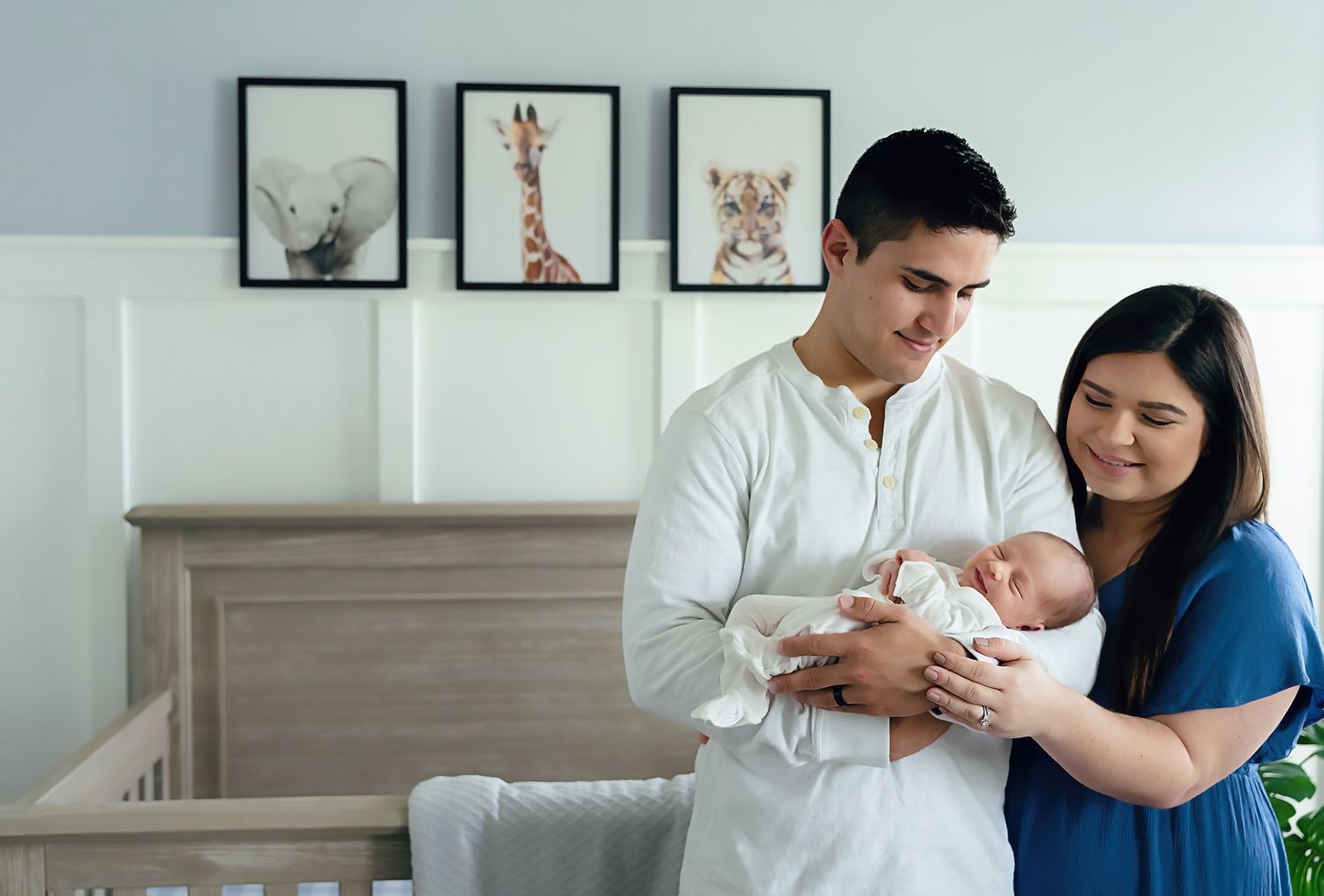 Dad cradling his smiling newborn in front of the babies crib as mom embraces them from the side during a Columbia SC in-home newborn session