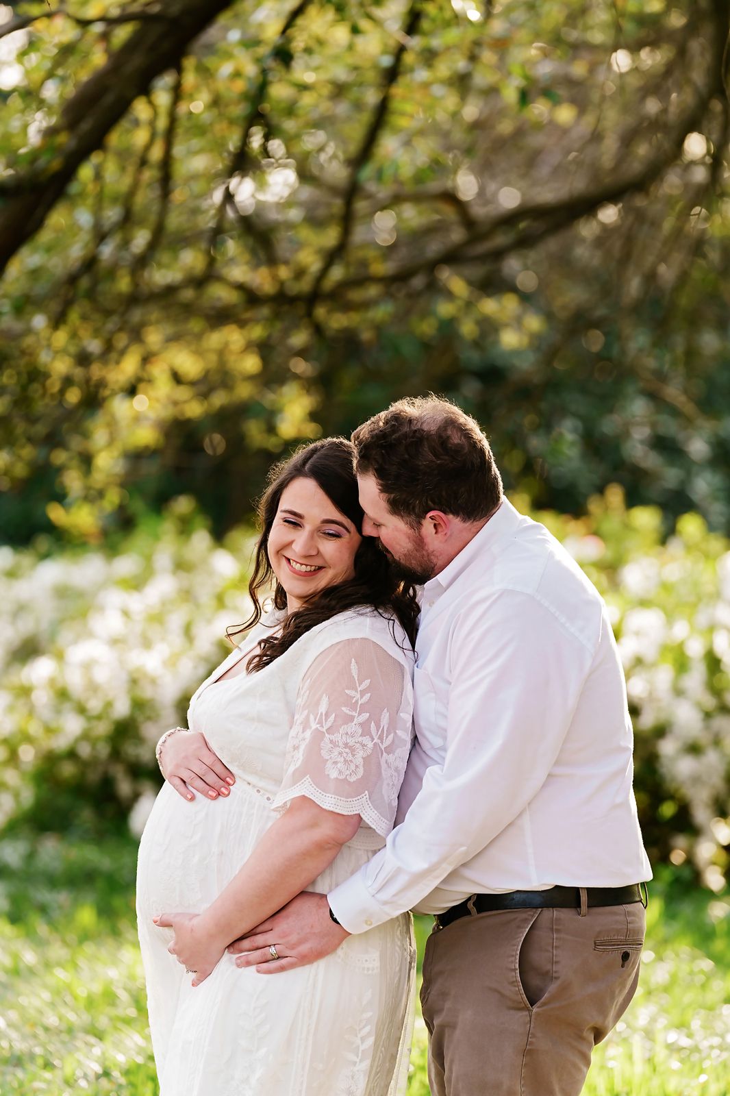 Mom and Dad to be lovingly embracing under a gorgeous tree with white flowers in background during a Columbia SC Maternity Portrait Session.