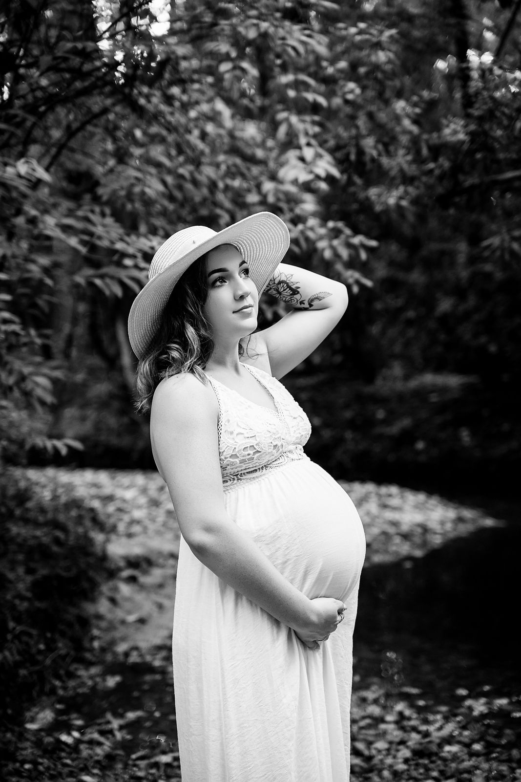 Black and White image of mom to be in a white dress against a creek setting during a Lexington SC Maternity Session.