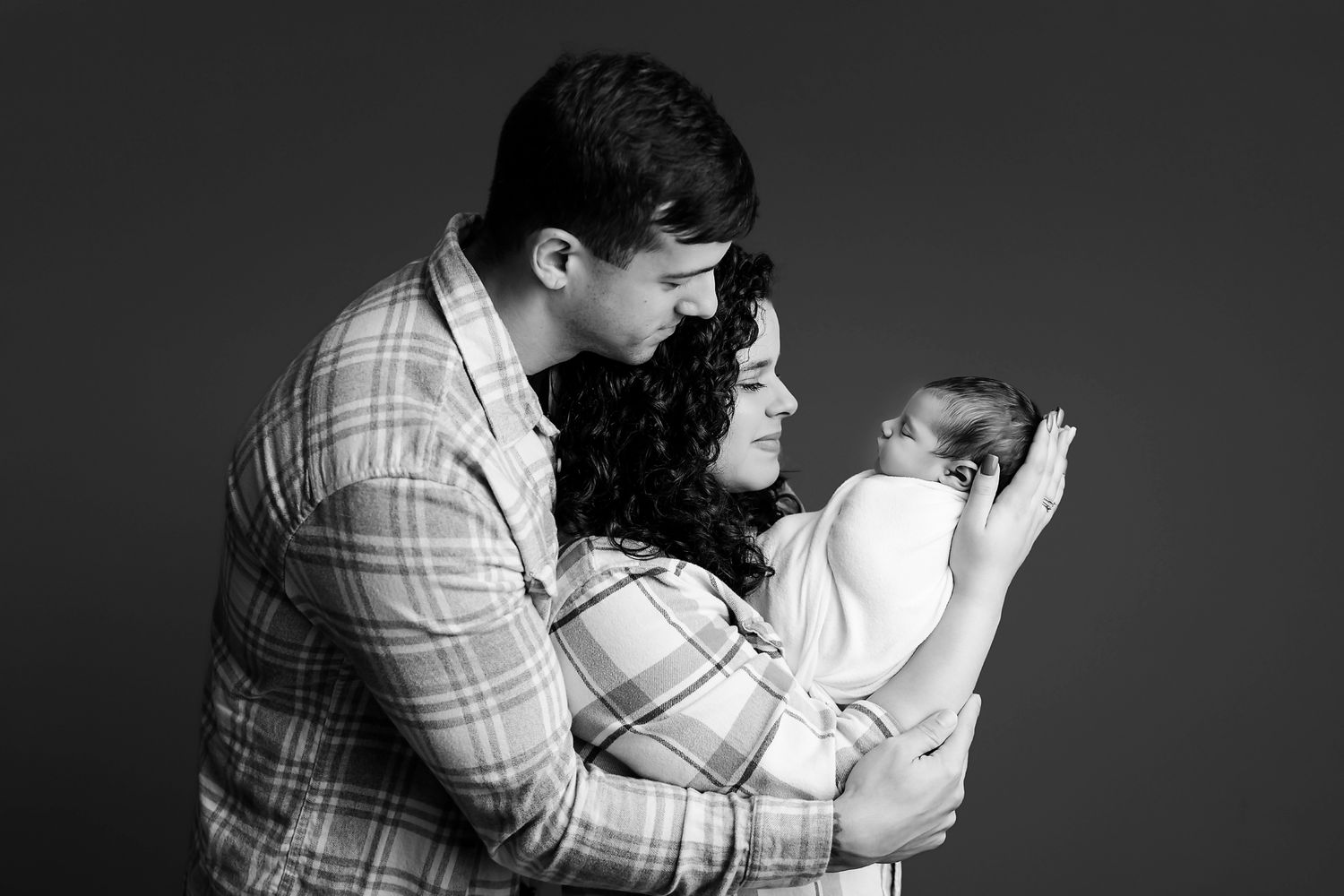 Intimate side profile black and white Chapin SC  studio newborn portrait of Mom and Dad looking at their newborn baby in moms arms.