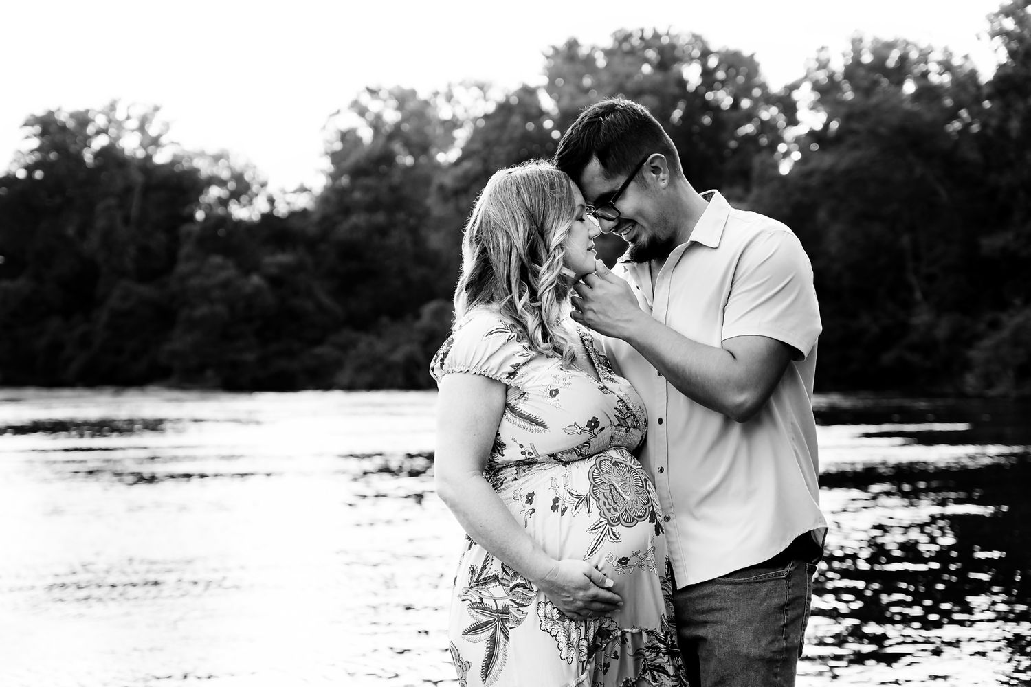 Maternity image showing Mom and Dad to be embracing in front of water as light reflects around them during a Maternity Session in Columbia.