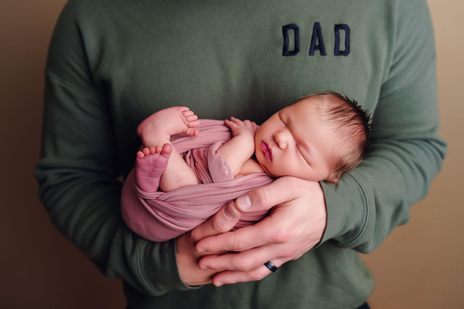 Closeup image of a sweet baby girl swaddled in a pink wrap and held in her daddy's hands taken during a studio Newborn Session in Chapin SC.