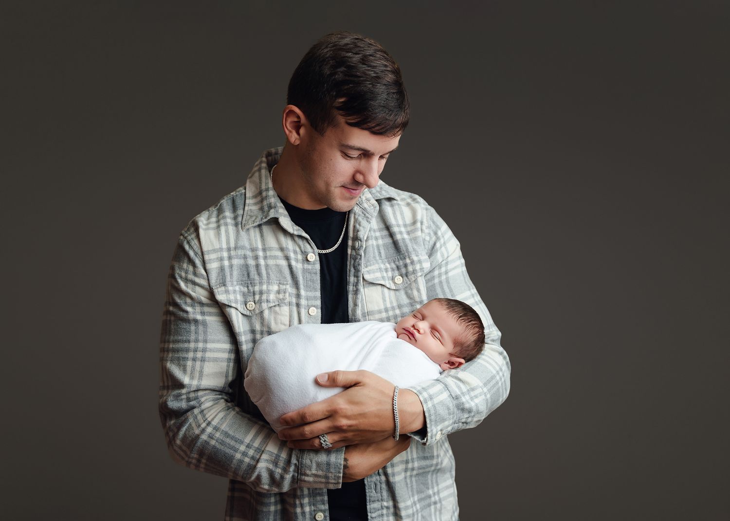 Dad cradling his newborn girl in his arms and lovingly looking down at her against a dark backdrop during a Studio Newborn Session in Chapin