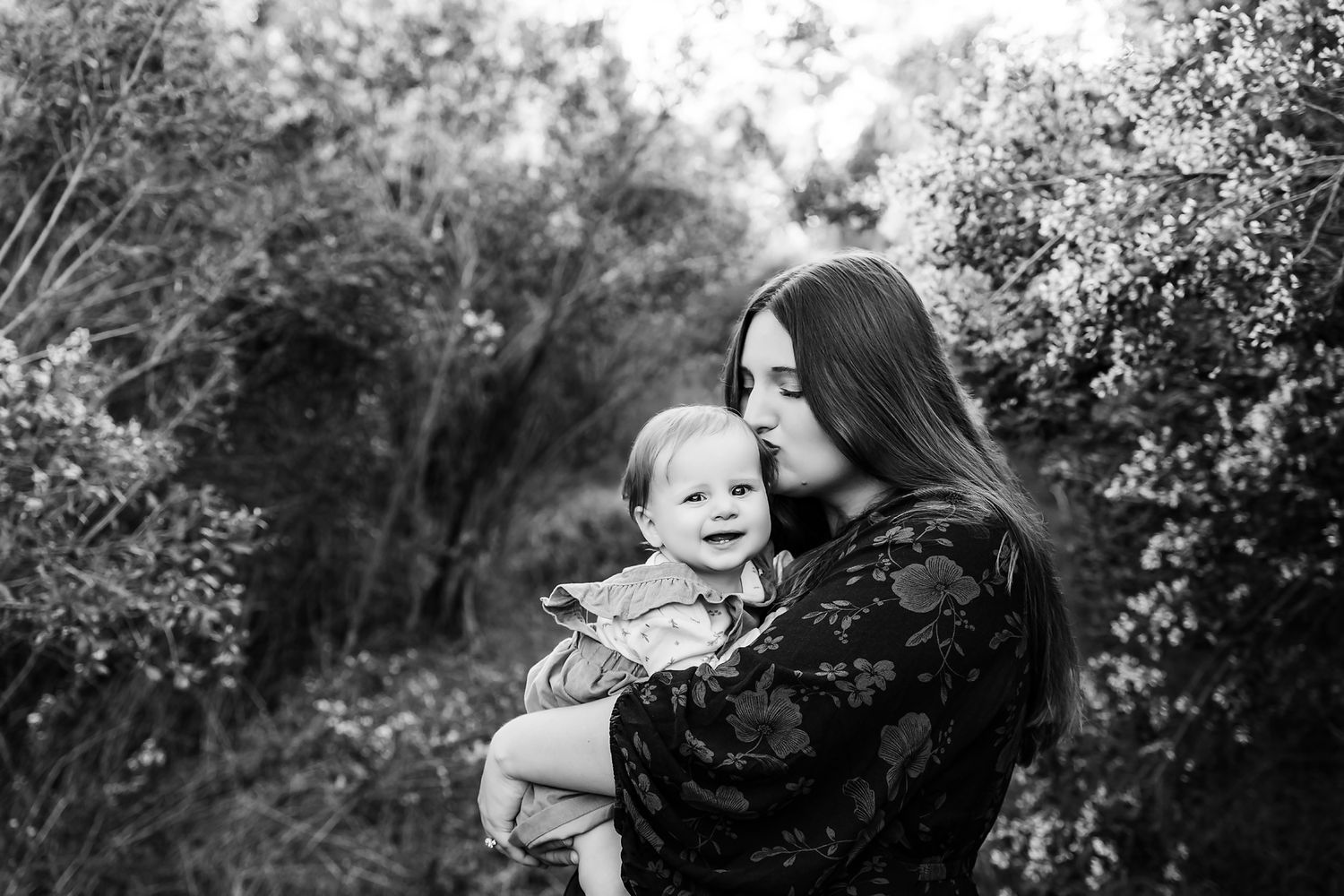 Black and White outdoors image of a Mom cradling her young baby as the baby smiles at the camera during a Columbia SC Motherhood Session.