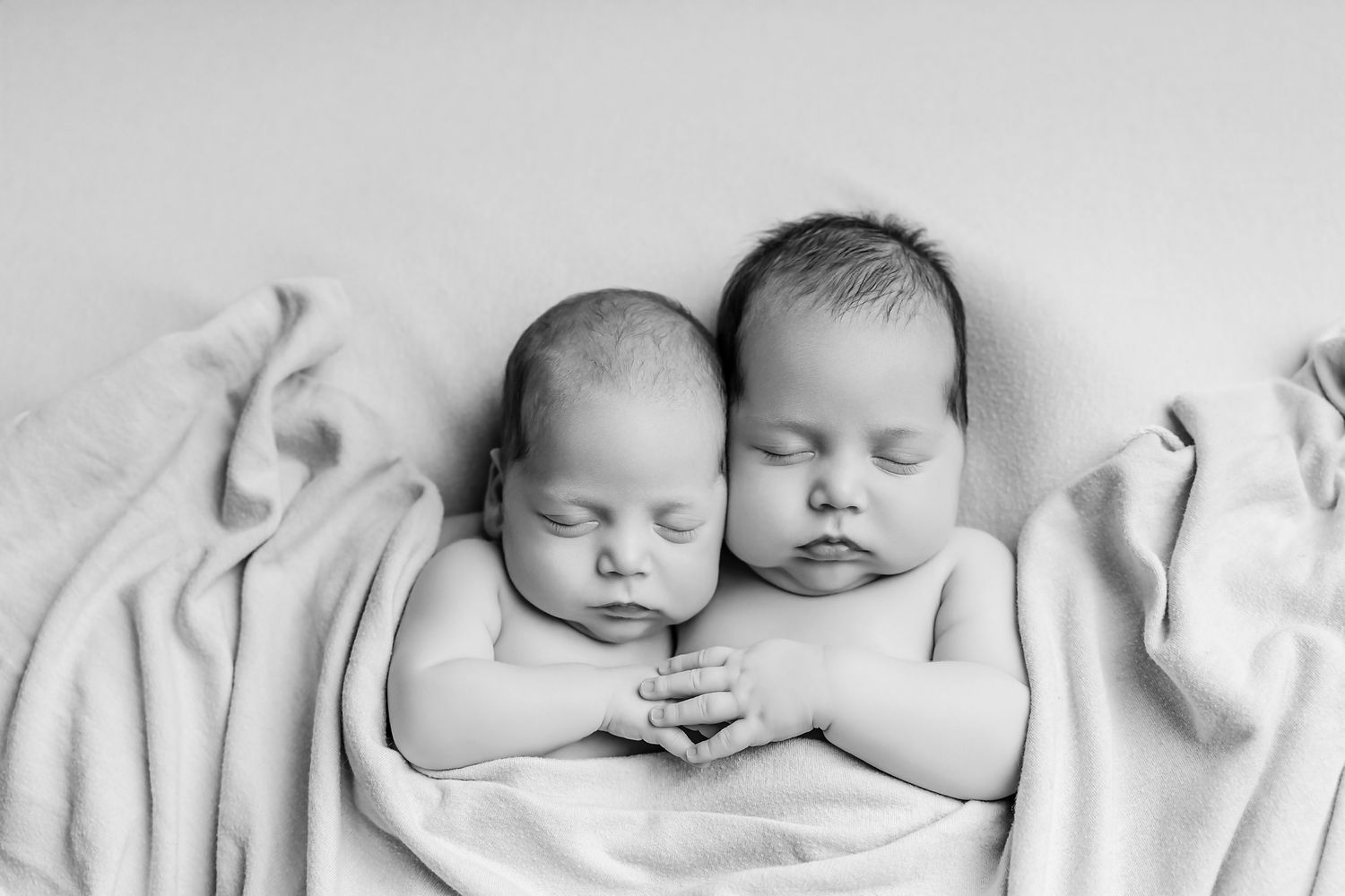 Black and White image of newborn twins cuddled together and holding hands during a studio portrait session for clients from Lexington SC.
