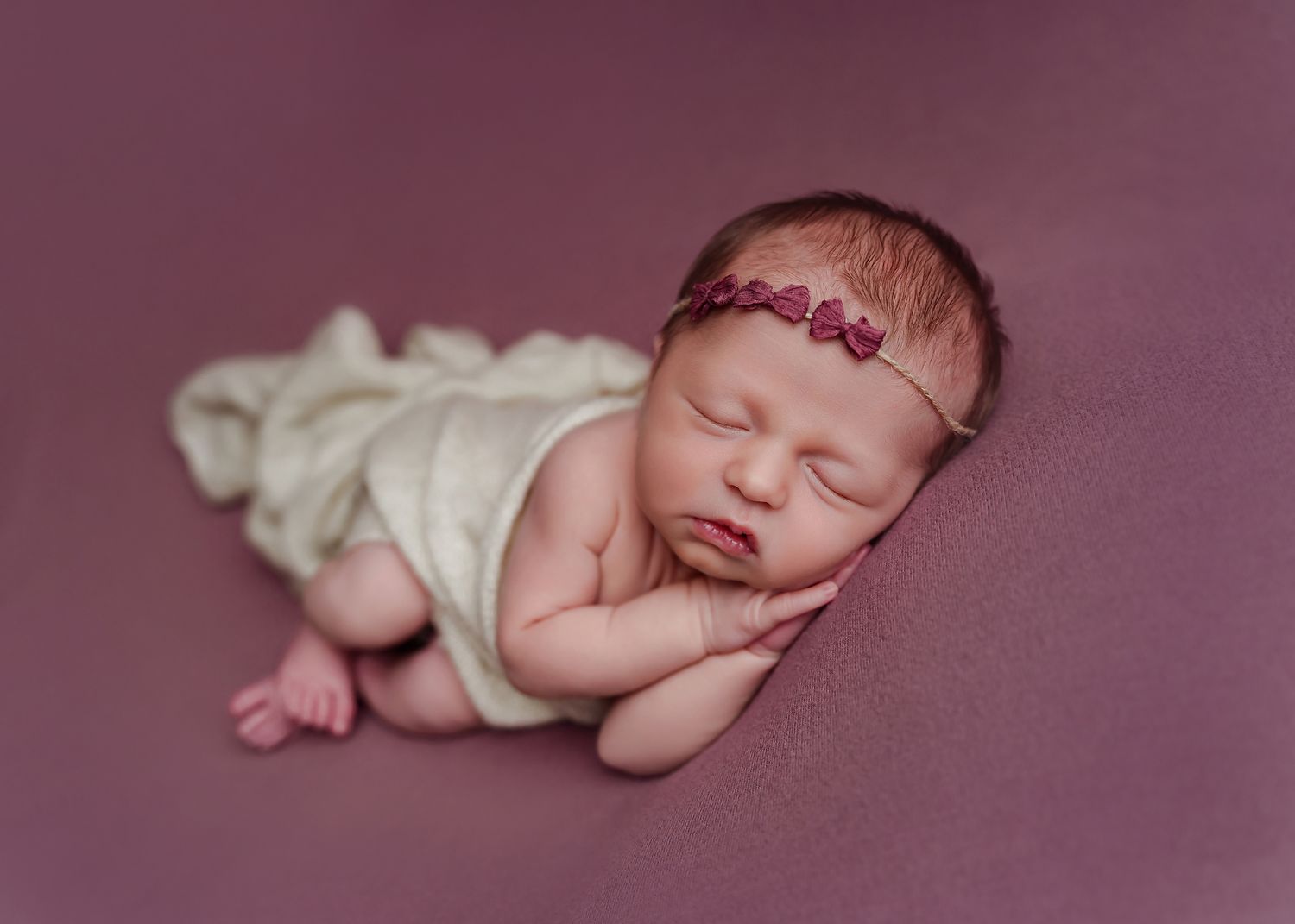 Newborn portrait of a baby girl posed on a plum colored backdrop and wrapped in a cream wrap during a Lexington SC Newborn Session.