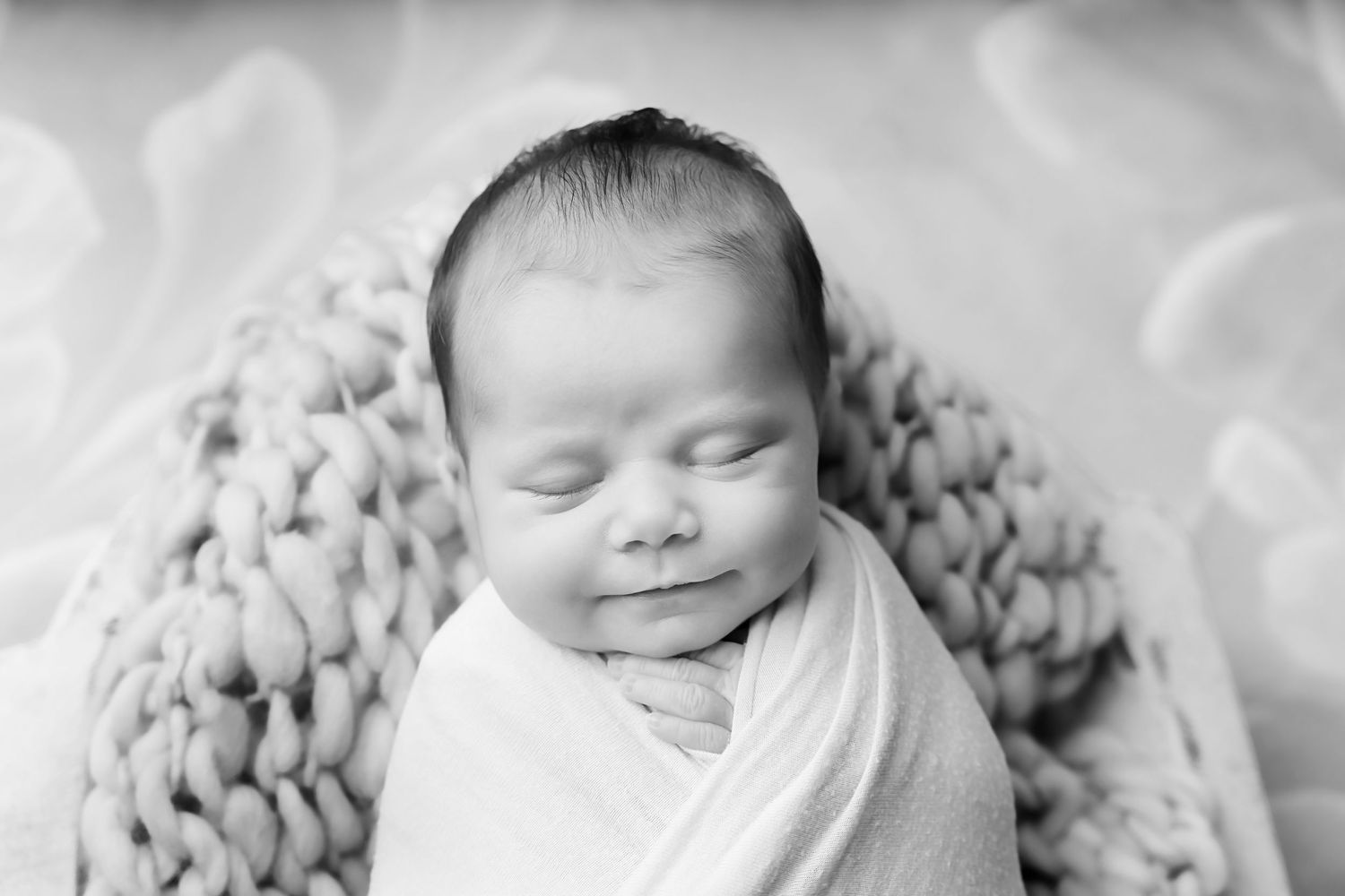 Black and White close-up image of a newborn baby swaddled and smiling during a Chapin SC Studio Newborn Session.