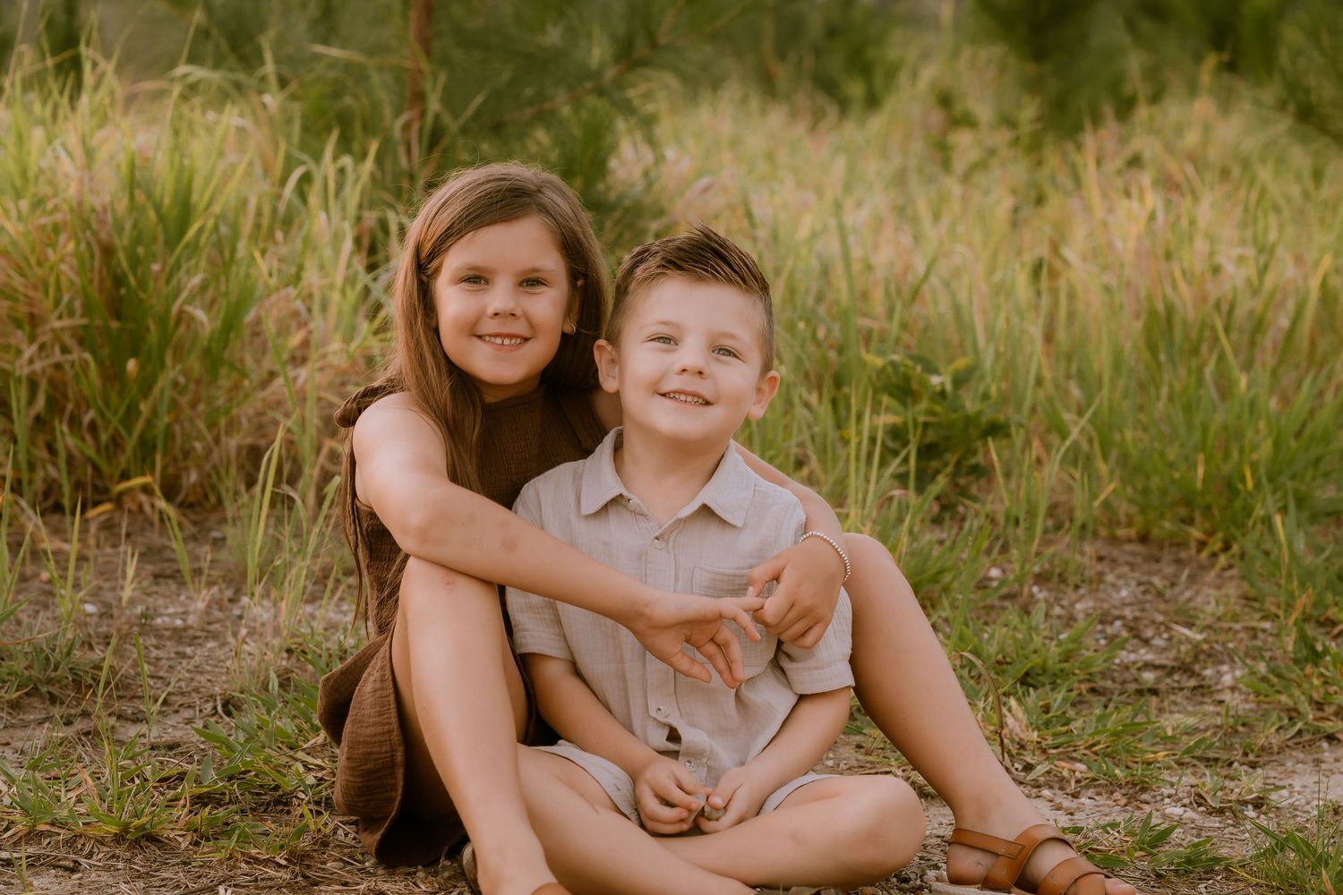 Brisbane family photographer — family of four sitting together in golden field with mountain backdrop, warm and relaxed lifestyle session by