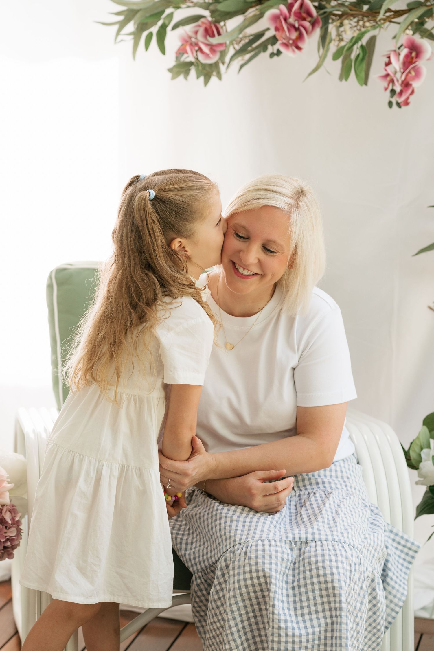 Brisbane family photography — grandmother seated with young granddaughter sharing a tender moment indoors, floral background, captured by Jo