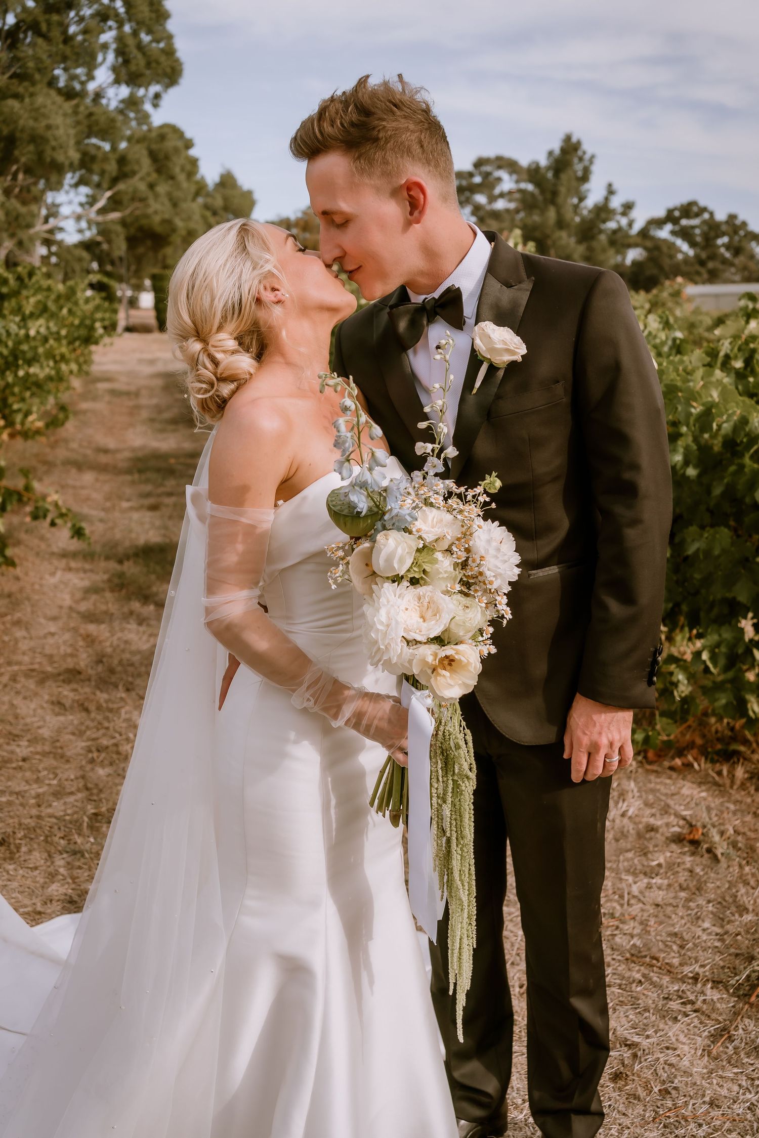 Brisbane wedding photographer — bride and groom sharing their first kiss outdoors surrounded by nature, genuine and joyful wedding celebrati
