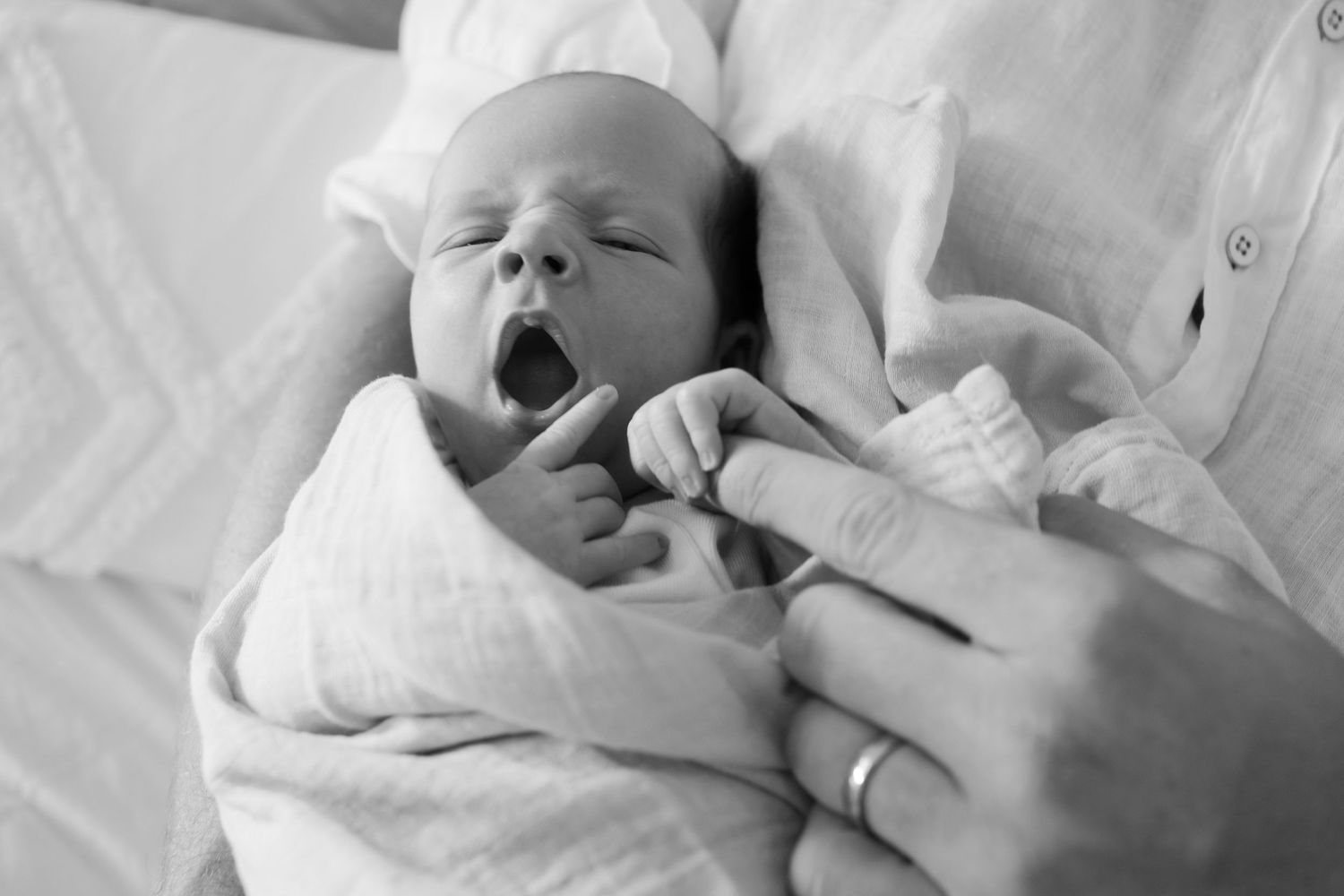 Brisbane newborn photographer — black and white close-up of newborn baby yawning with tiny fist raised, adorable and candid in-home session