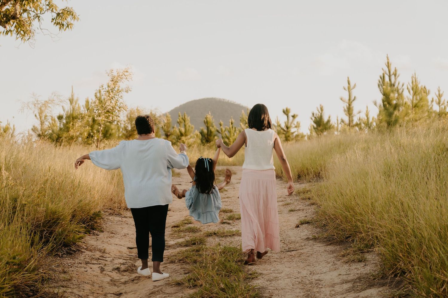 Brisbane family photographer — family of four walking hand in hand along a golden field path from behind, beautiful lifestyle session by Joy