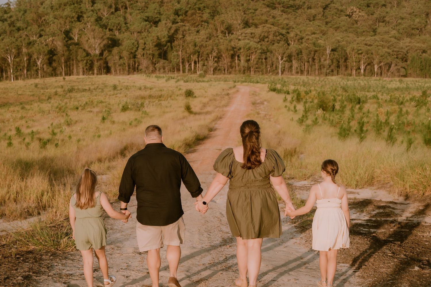 Brisbane family photographer — parents and children walking together along a golden field path at sunset, lifestyle family session by Joy Fi