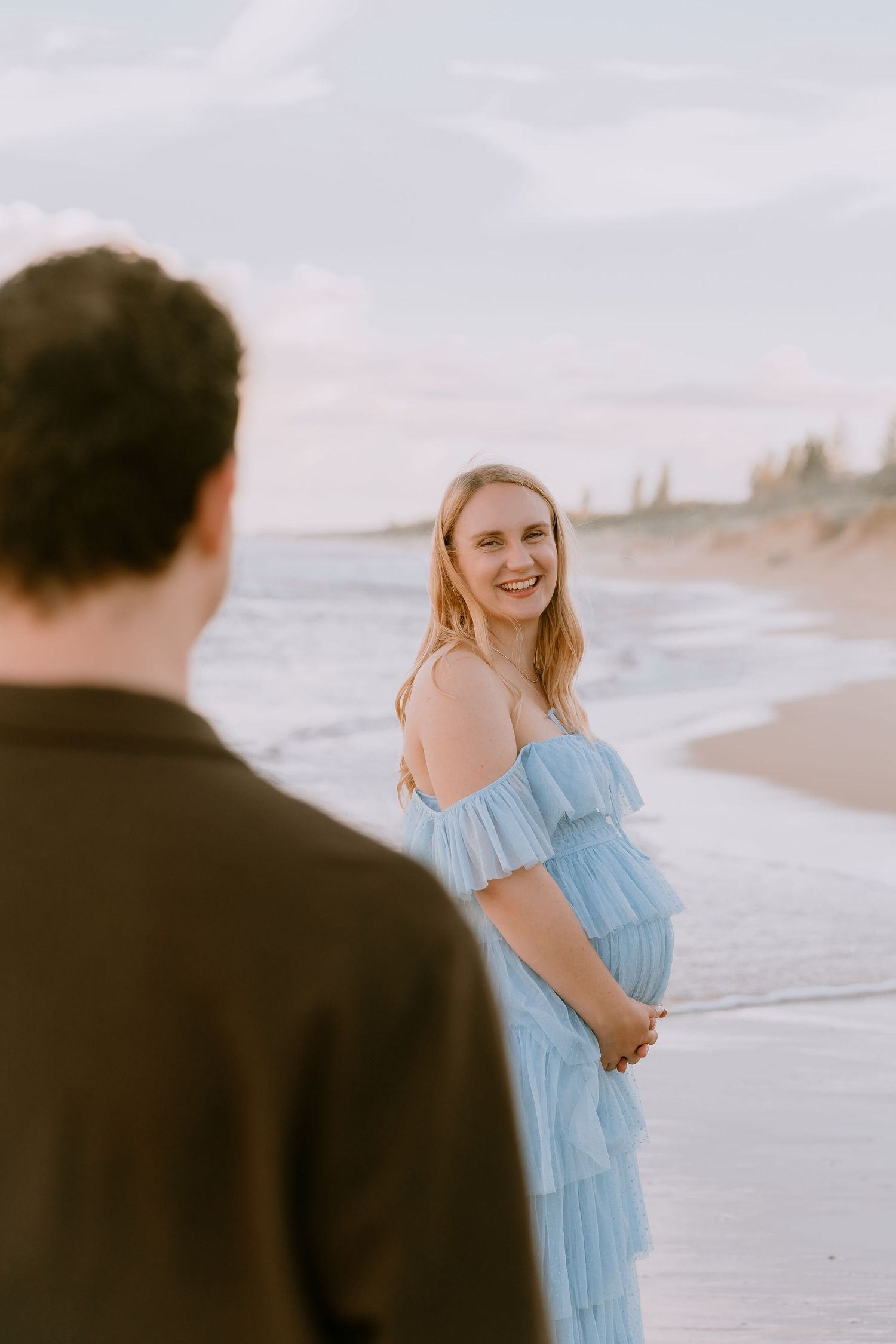 Brisbane maternity photographer — couple standing together by the ocean, man looking at his partner lovingly during a coastal maternity sess