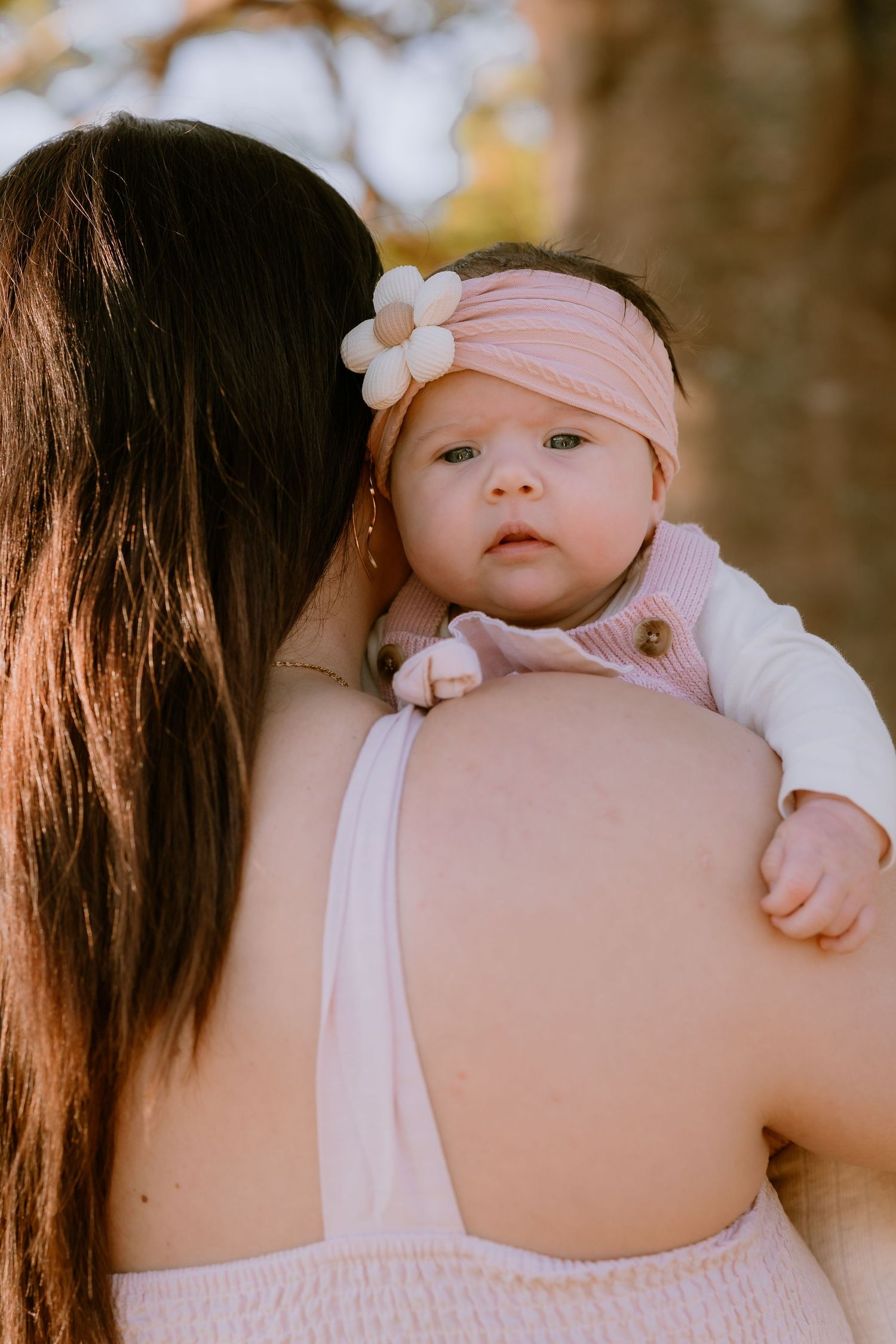 Brisbane family photographer — mother holding her baby over her shoulder outdoors in warm afternoon light, candid and loving family portrait