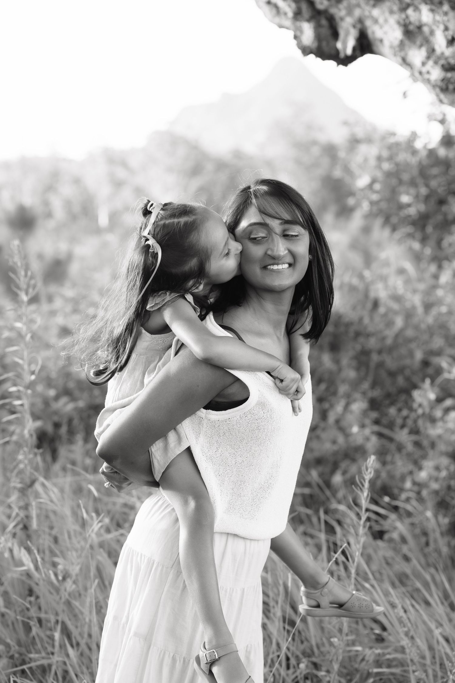 Brisbane family photographer capturing candid black and white moment of mother laughing and cuddling child outdoors in natural light — Joy F
