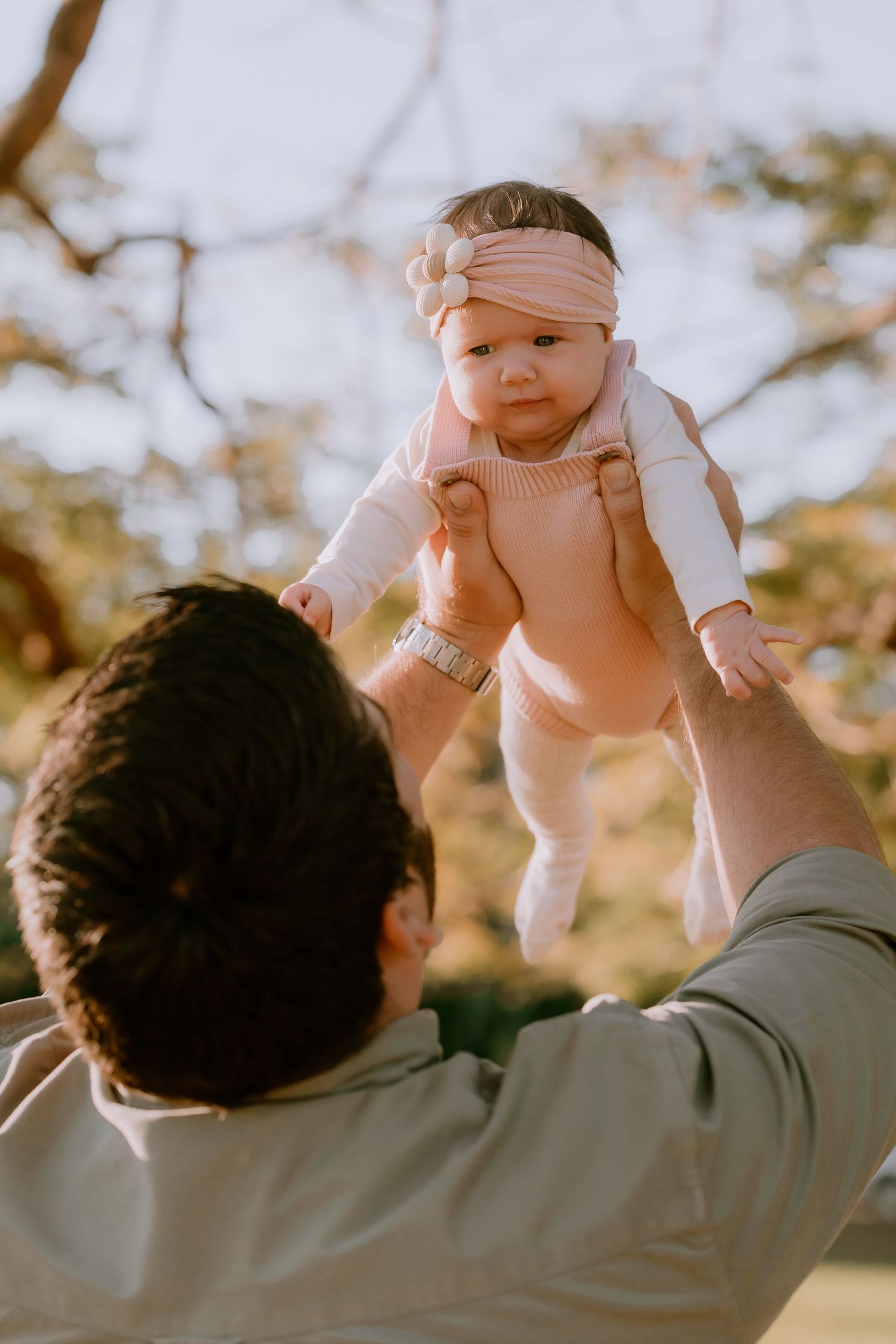 Brisbane family photographer — parent lifting baby high in the air at golden hour, pure joy and laughter captured in a candid family lifesty