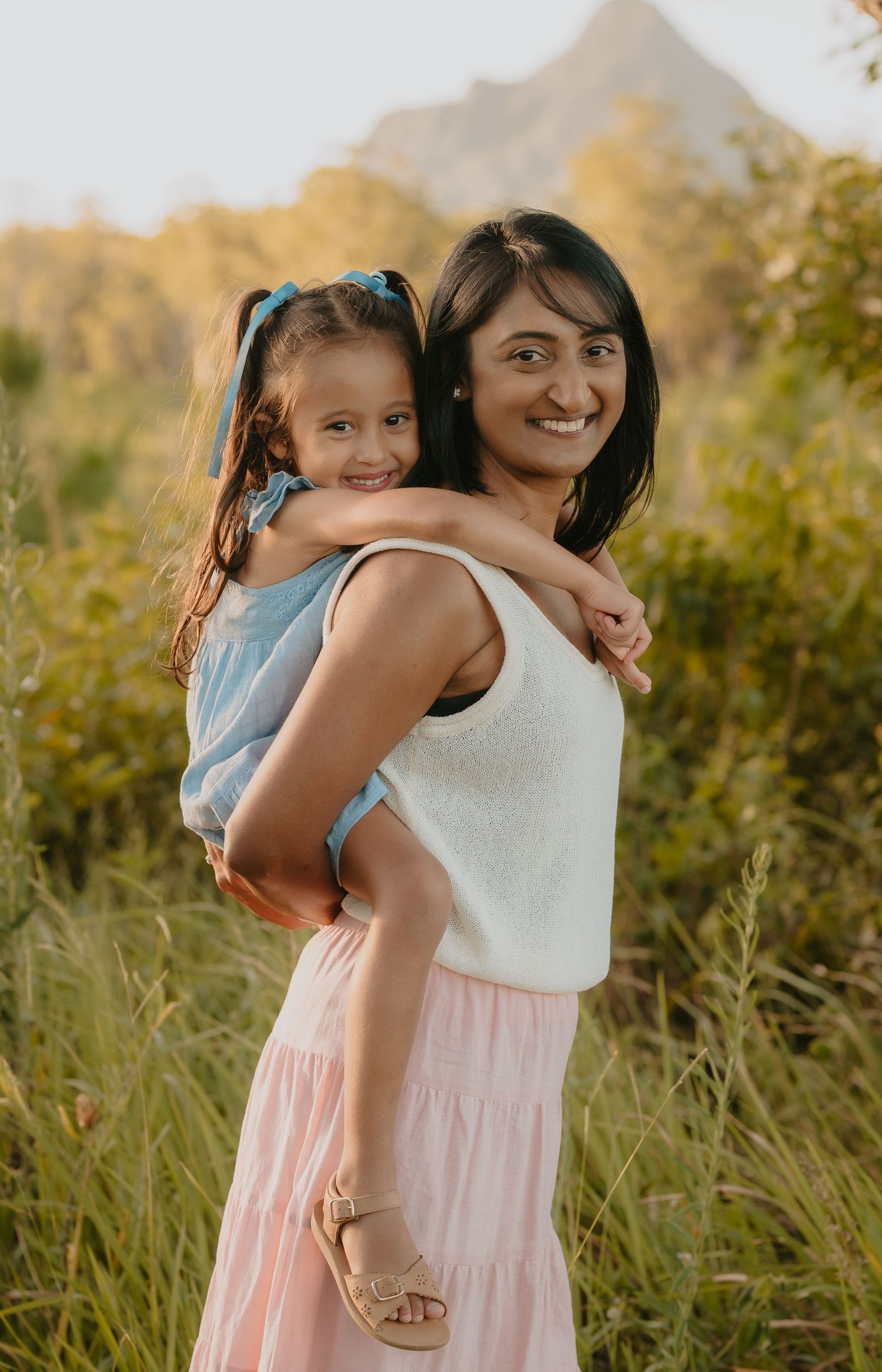 Brisbane family photographer — mother holding and cuddling young child outdoors in warm golden light, candid family portrait by Joy Filled P