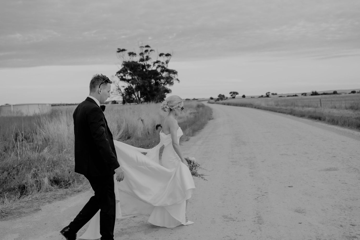 Brisbane wedding photographer — black and white image of bride and groom walking hand in hand along a country road, relaxed and romantic wed