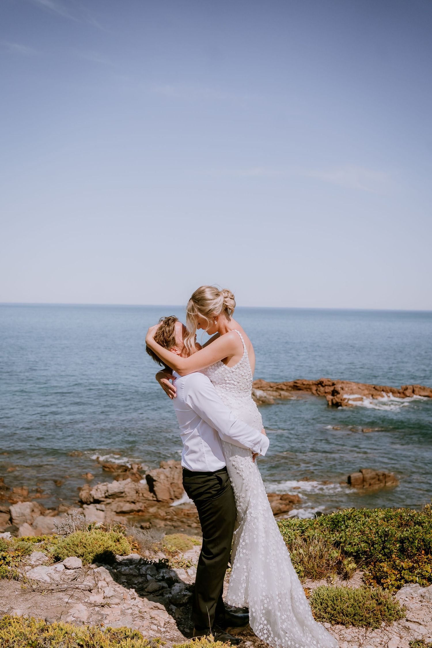 Brisbane elopement photographer — groom lifting bride joyfully with ocean and cliffs behind them, exhilarating and romantic coastal elopemen