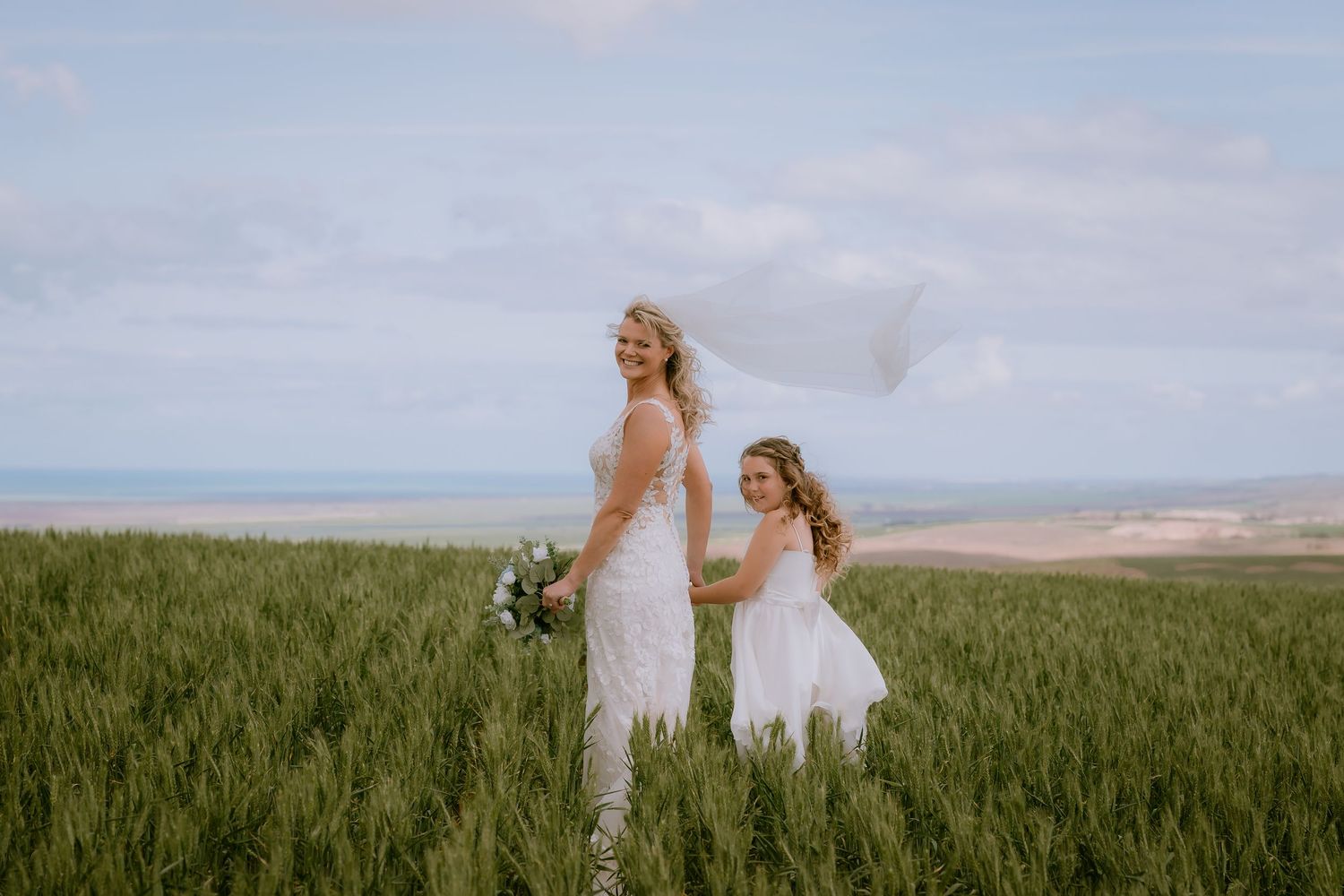 Brisbane wedding photographer — bride standing alone in an open green field holding her bouquet, dreamy and editorial bridal portrait by Joy