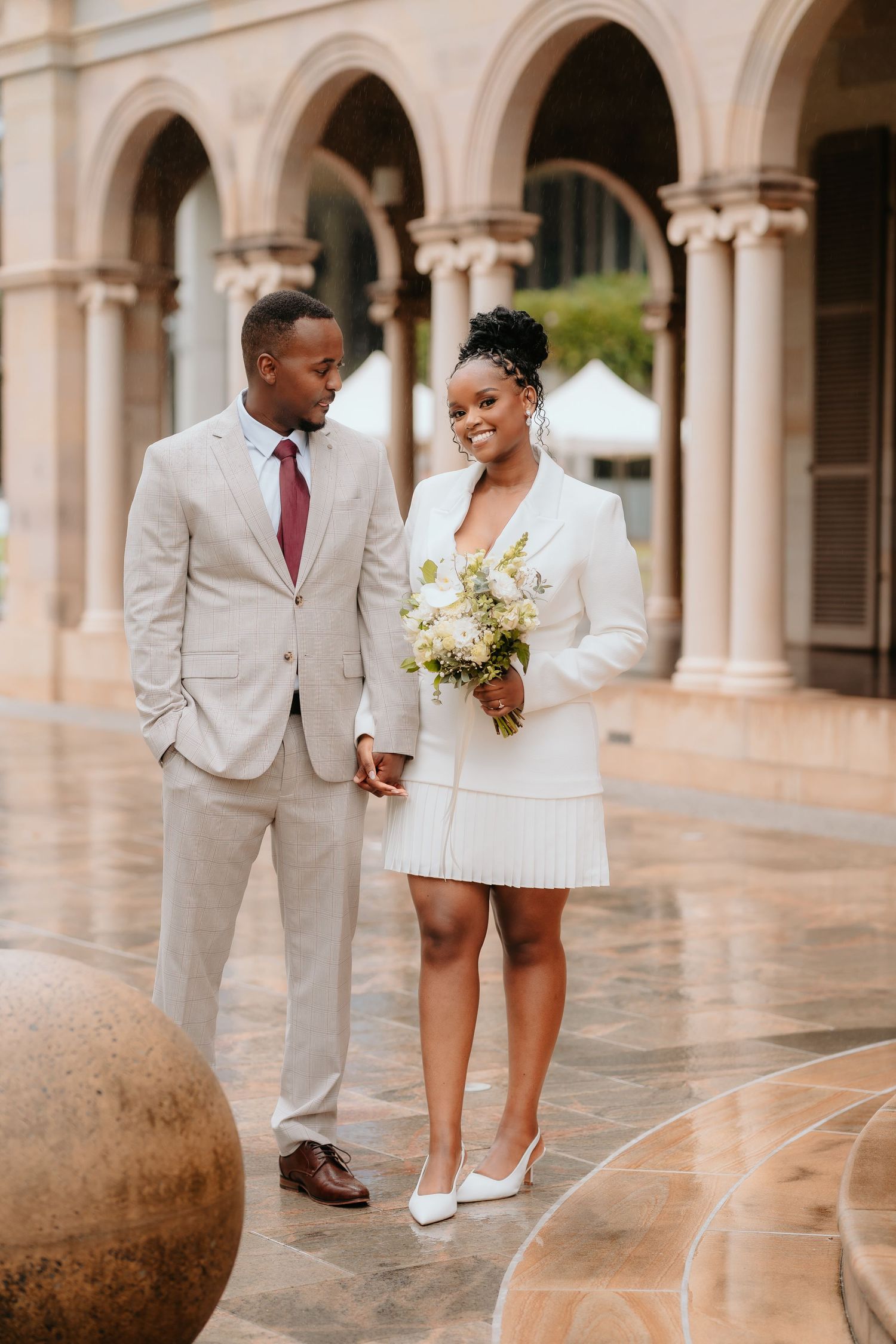 Brisbane wedding photographer — bride and groom walking through elegant venue archway, relaxed and joyful outdoor wedding portrait by Joy Fi