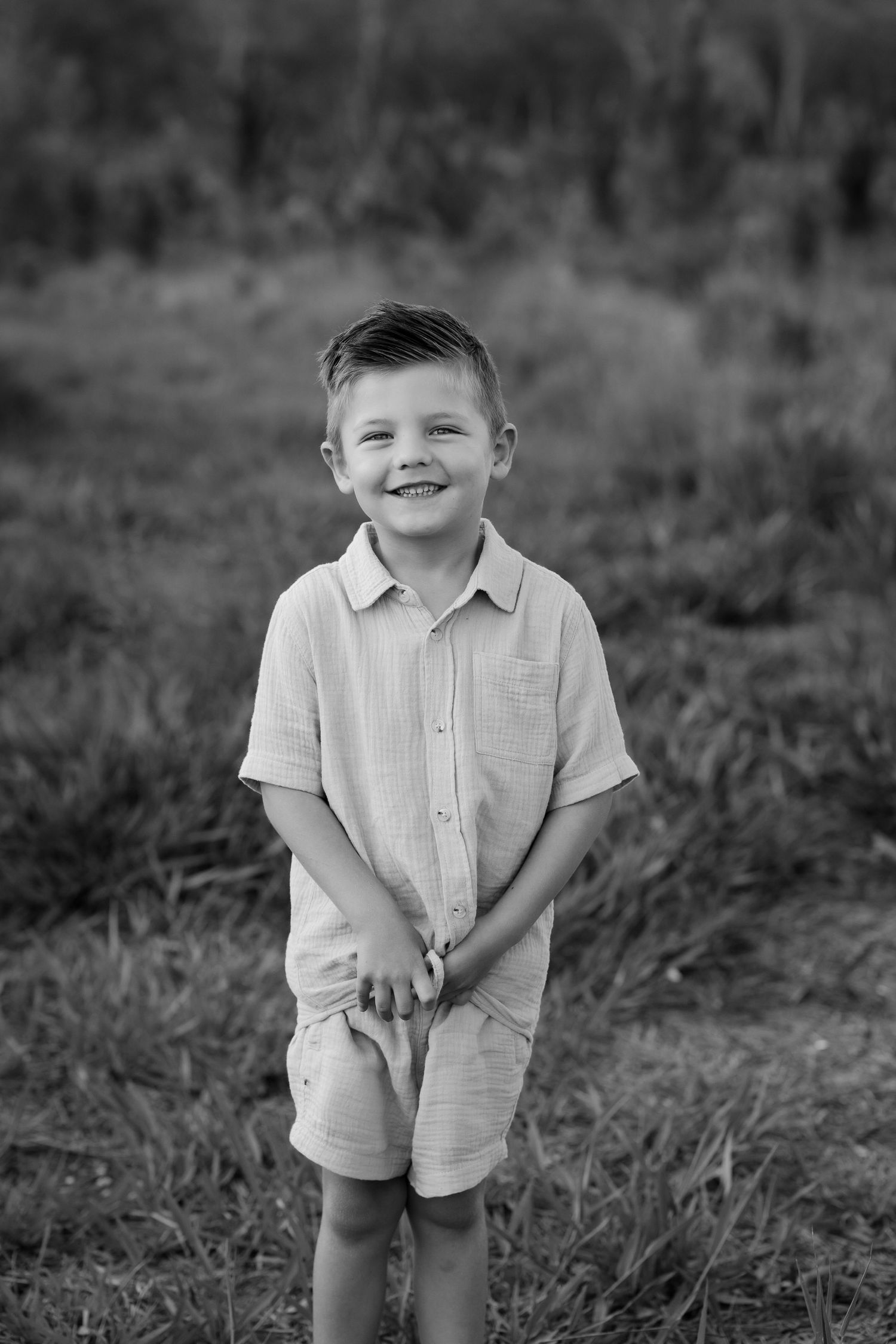 Brisbane family photographer — candid black and white portrait of a young boy smiling in a grassy outdoor setting, captured by Joy Filled Ph