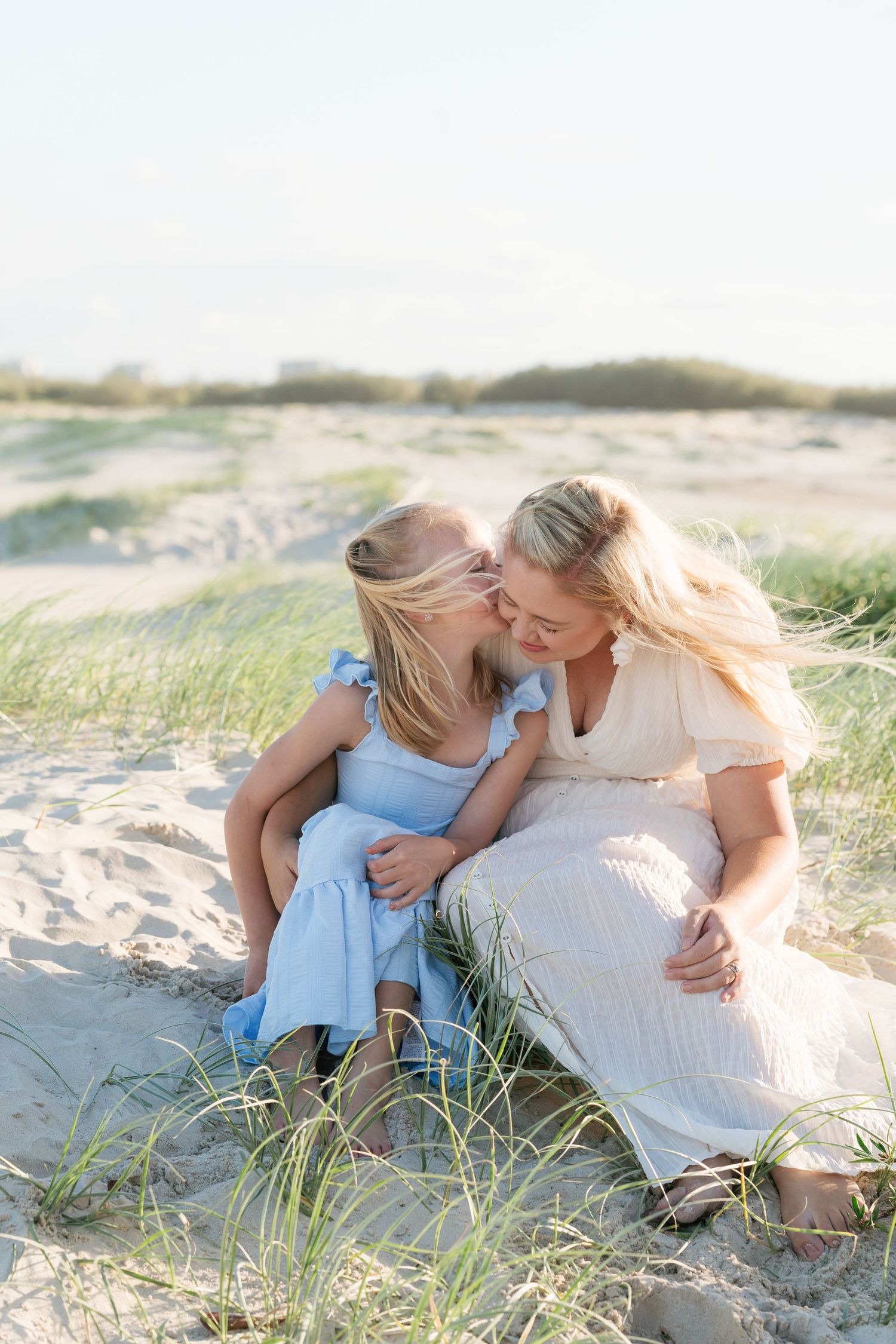 Brisbane family photographer — older mother and adult daughter sharing an affectionate moment sitting on sand dunes, heartfelt family portra