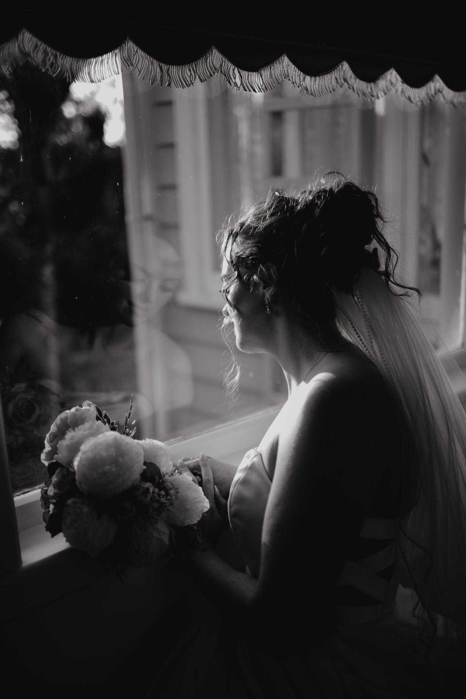 Dramatic black and white silhouette of a bride in a veil backlit by window light creating a romantic mood.