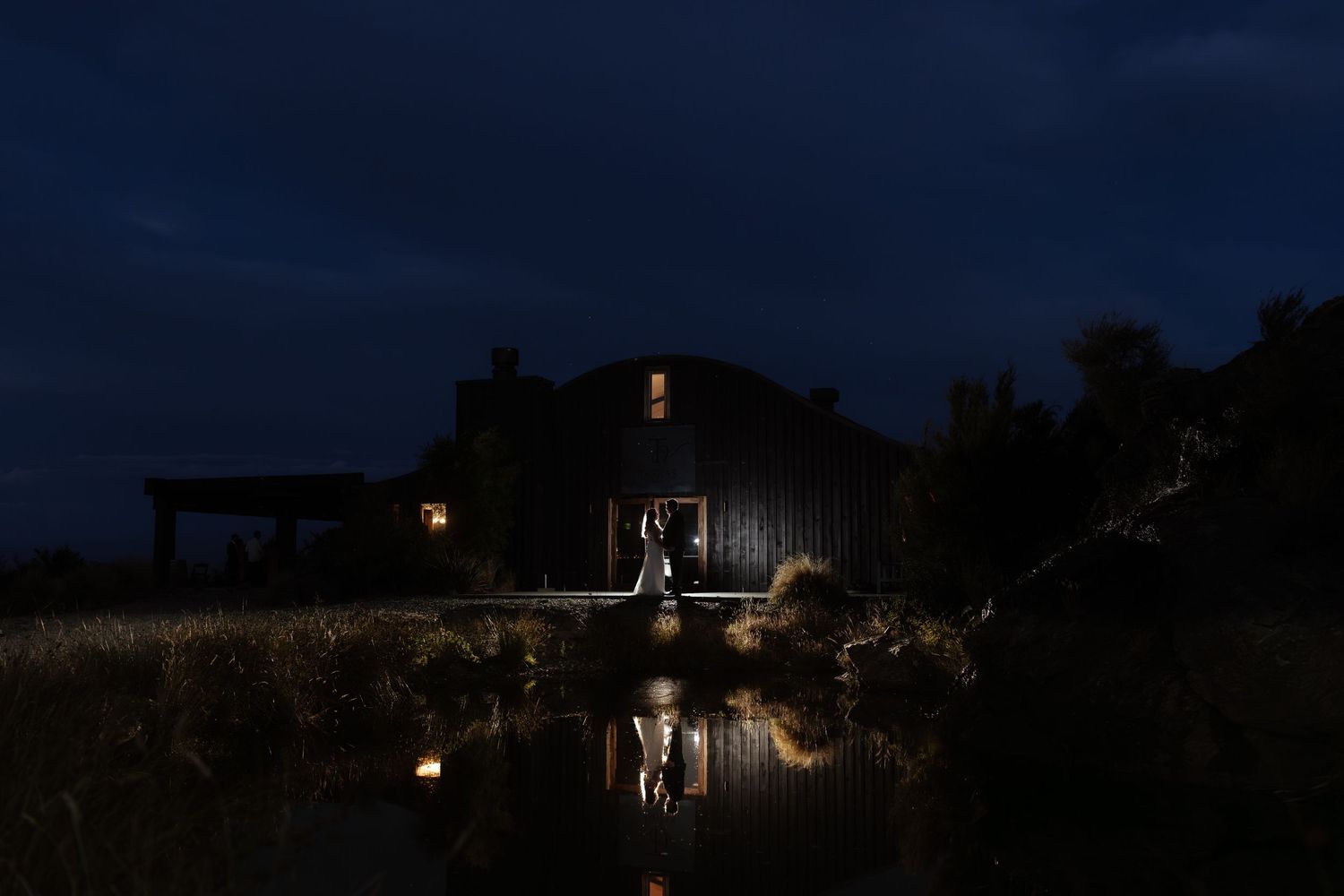 Silhouetted figures walk along a dark path illuminated by warm glowing lights in a romantic evening setting.