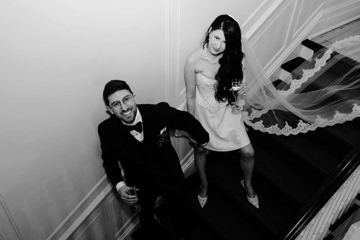 Black and white photo of a playful couple posing on stairs at their wedding at Paletta Mansion.