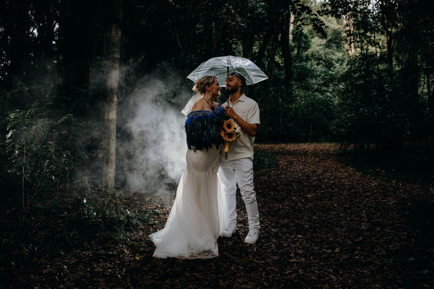 A couple in wedding attire shares an intimate moment in a misty forest setting.