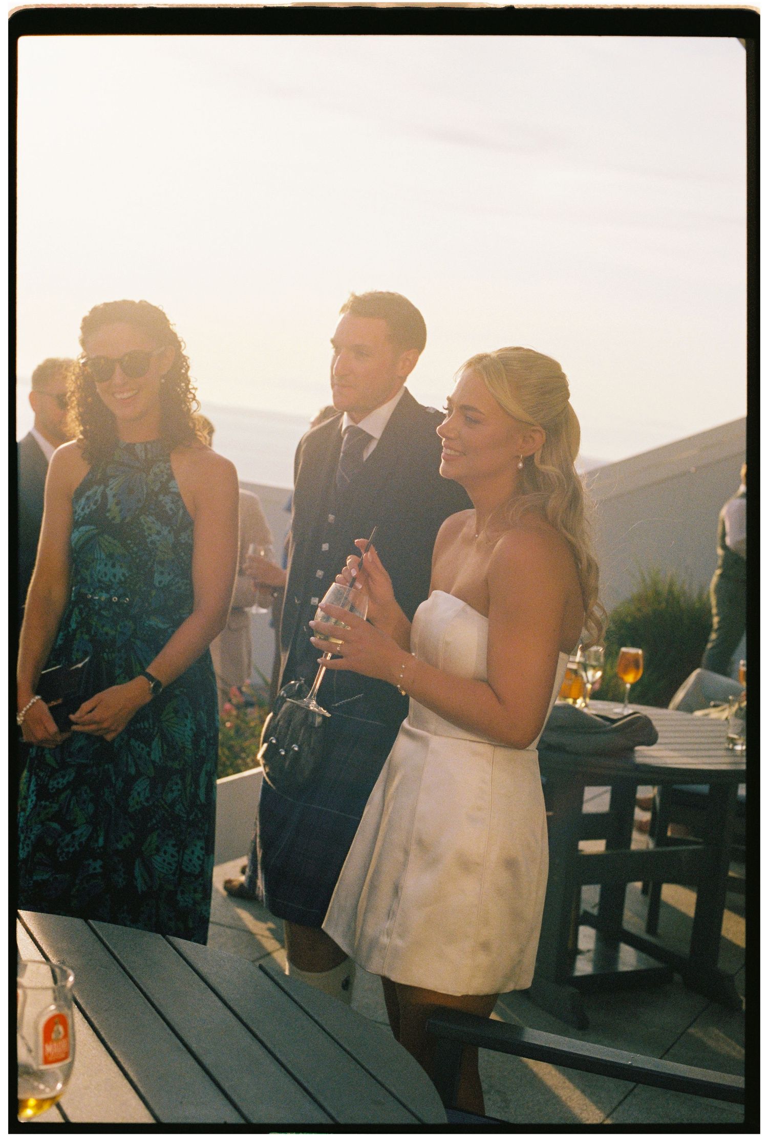 Guests in formal attire socializing outdoors at a wedding reception during golden hour.