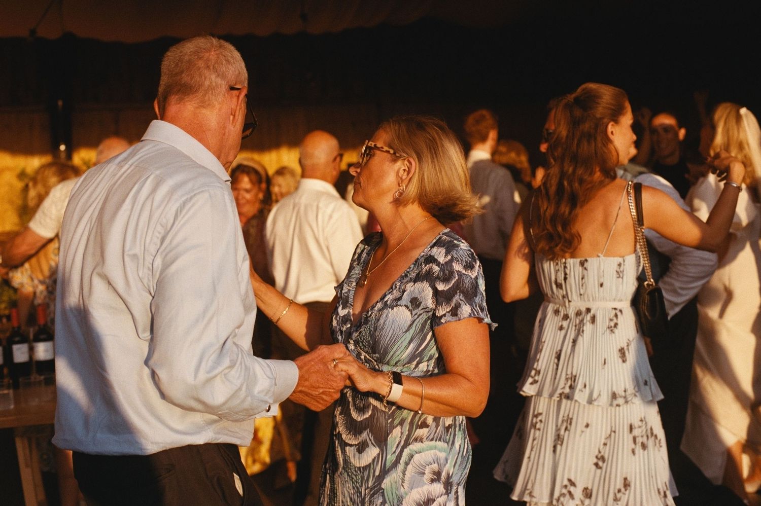 Couple dancing together at an outdoor evening wedding reception party with guests in background.
