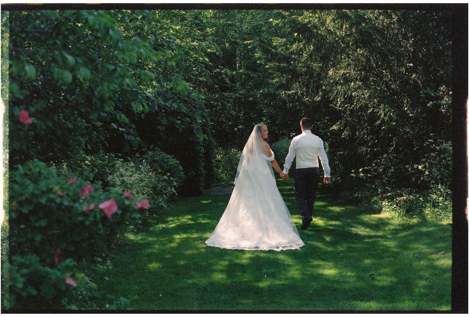 Bride and groom walking hand in hand through a lush green garden path on their wedding day.