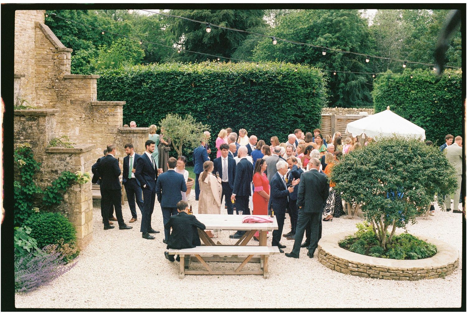 Elegant outdoor wedding reception in a lush garden courtyard with guests mingling on a gravel path.