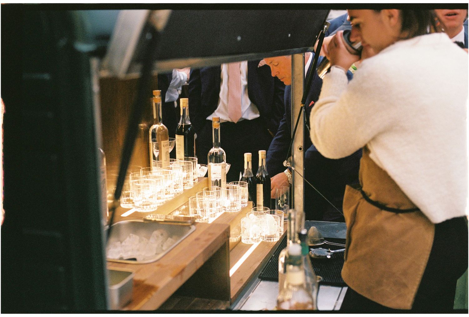 Bartender arranging wine bottles and glassware on a illuminated bar counter at an upscale event.