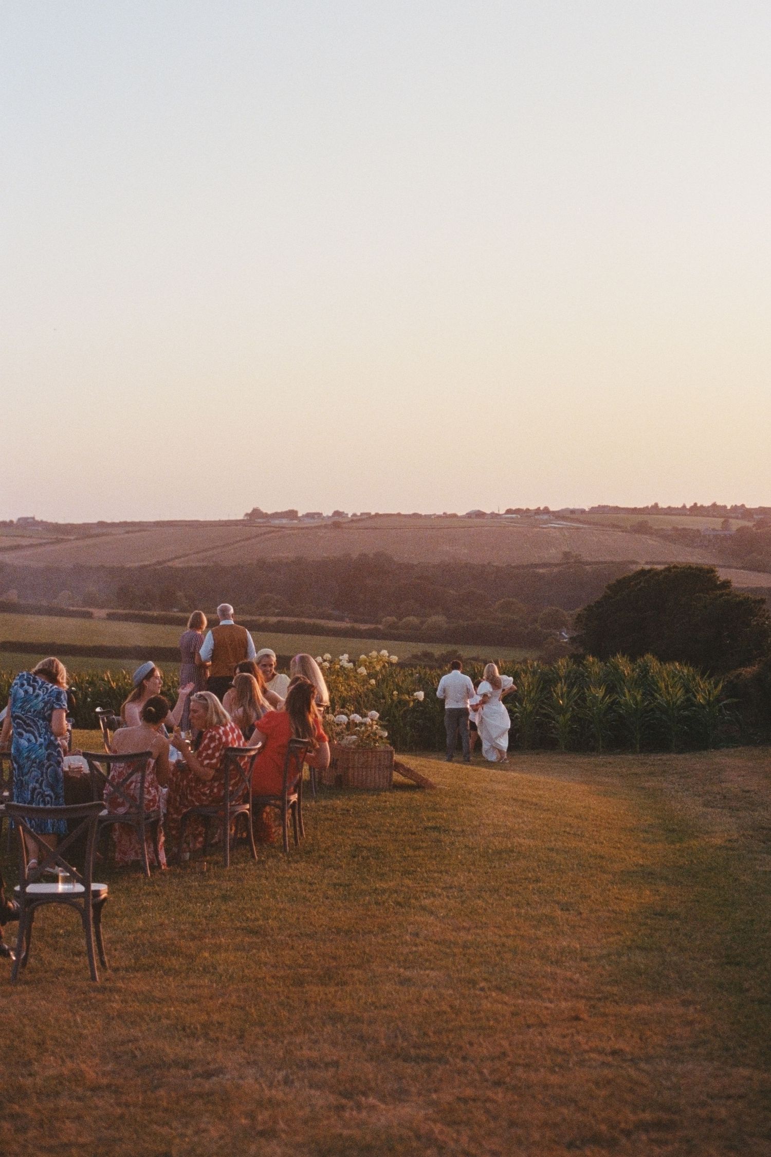 Wedding guests seated outdoors at golden hour overlooking rolling countryside hills at sunset ceremony.