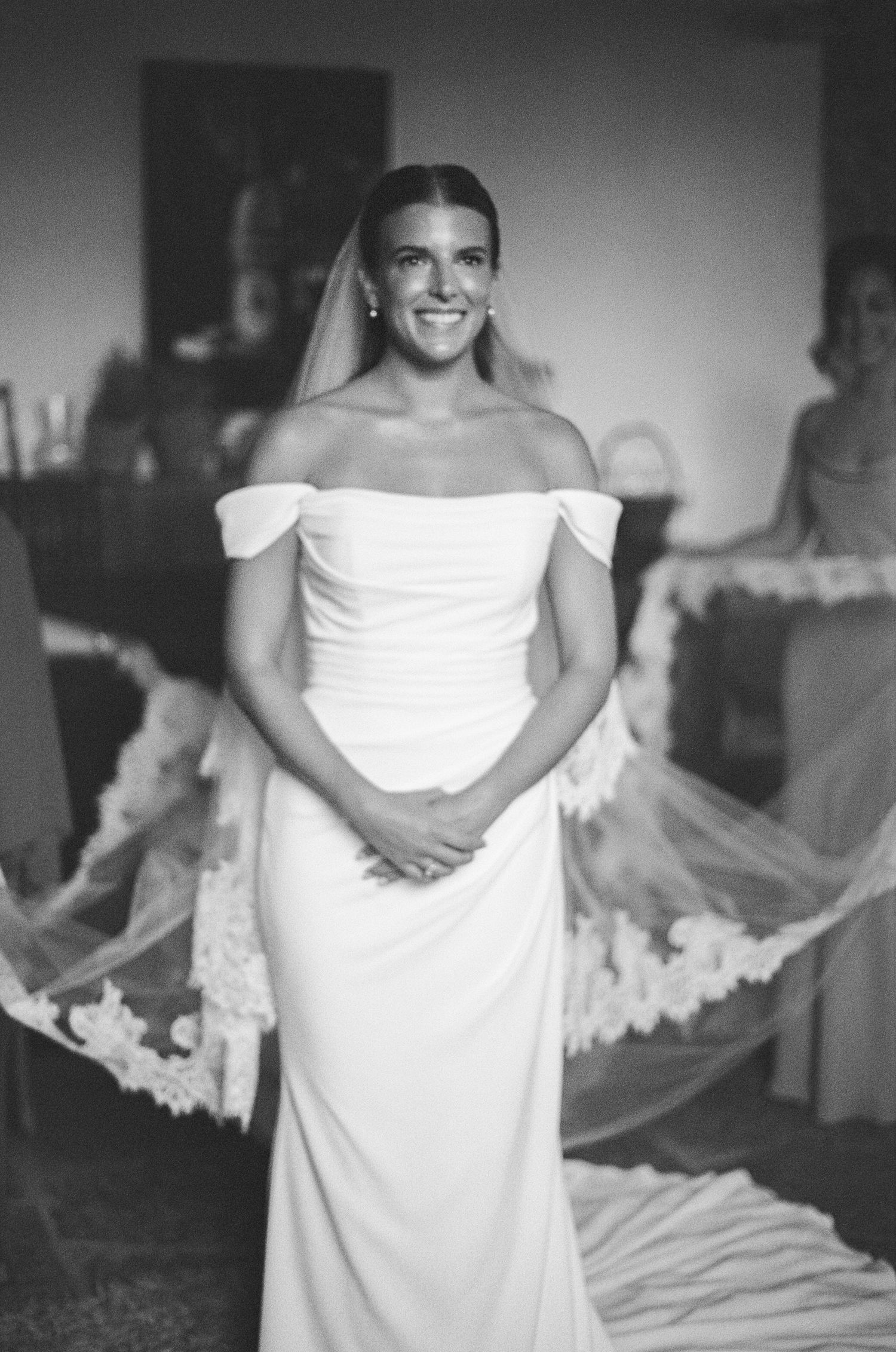 Radiant bride in off-shoulder white gown with lace-trimmed cathedral veil, black and white portrait.