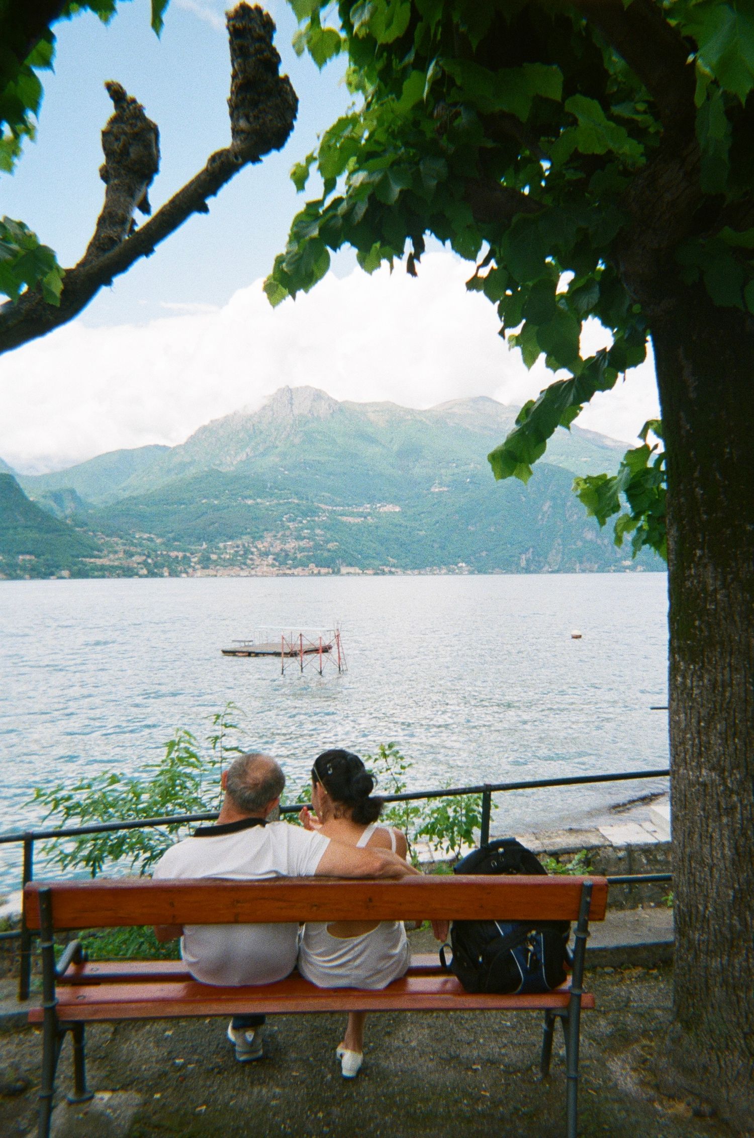 Couple sitting on a bench overlooking a serene mountain lake with scenic views.