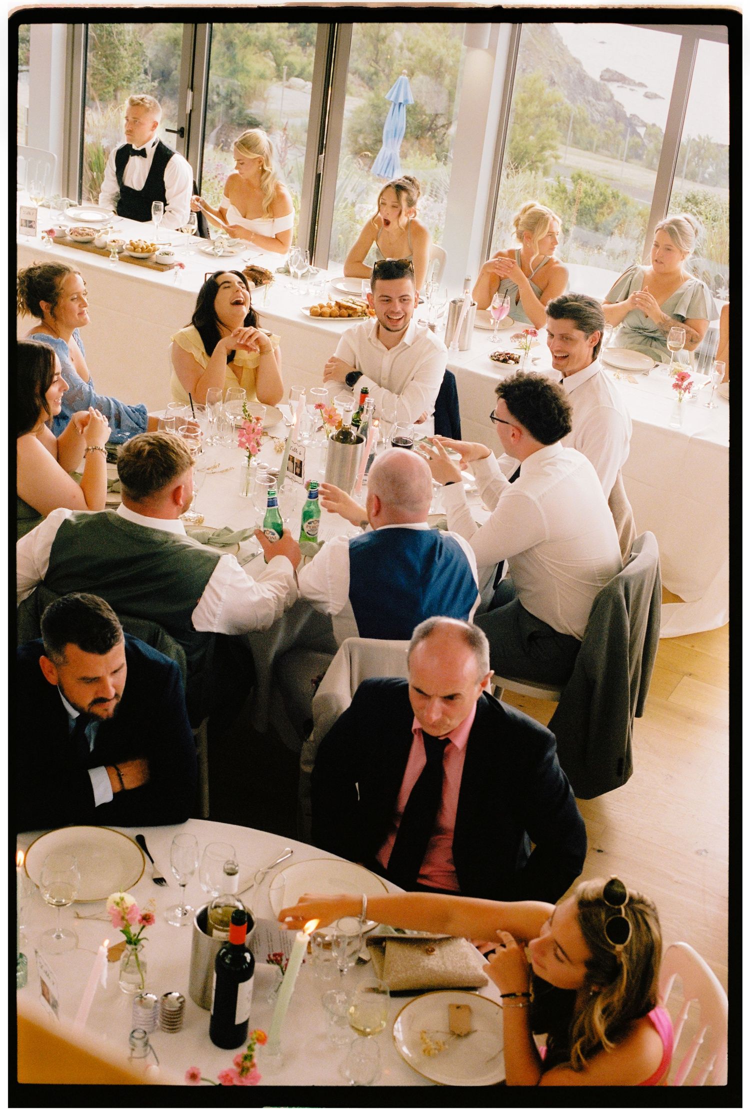 Aerial view of elegantly dressed wedding guests dining and socializing at round tables during a reception.