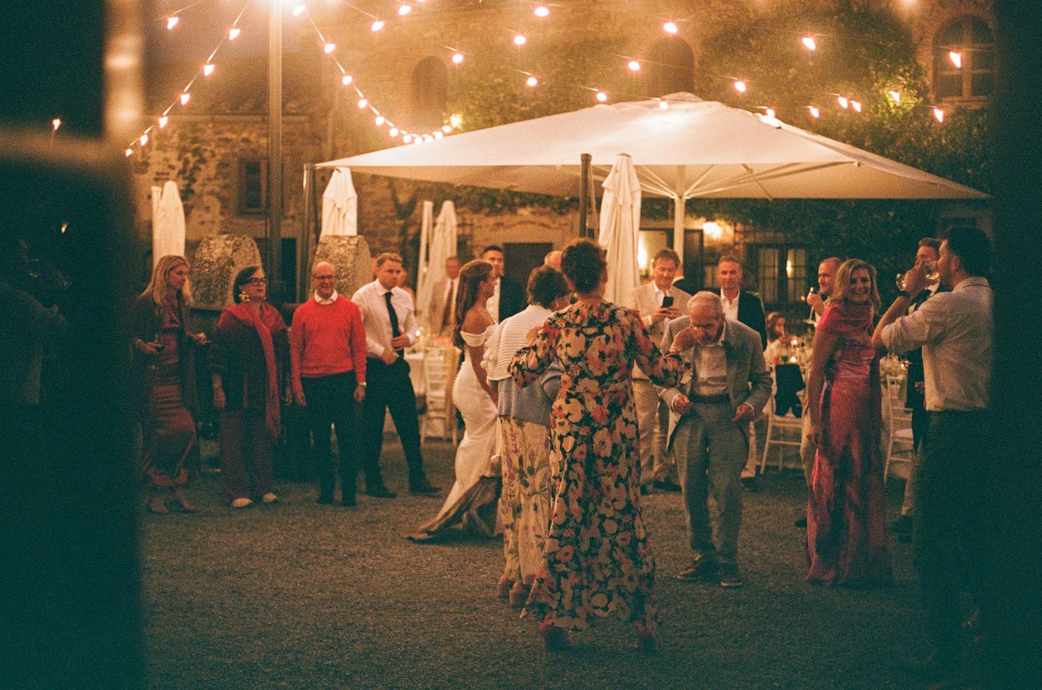 Guests dancing under warm string lights at romantic outdoor Tuscan wedding reception at night.