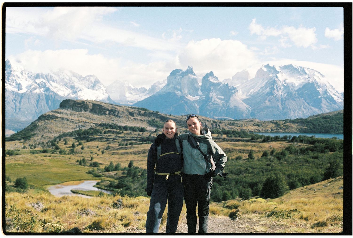Two hikers posing with backpacks in front of dramatic Torres del Paine mountain peaks in Patagonia.