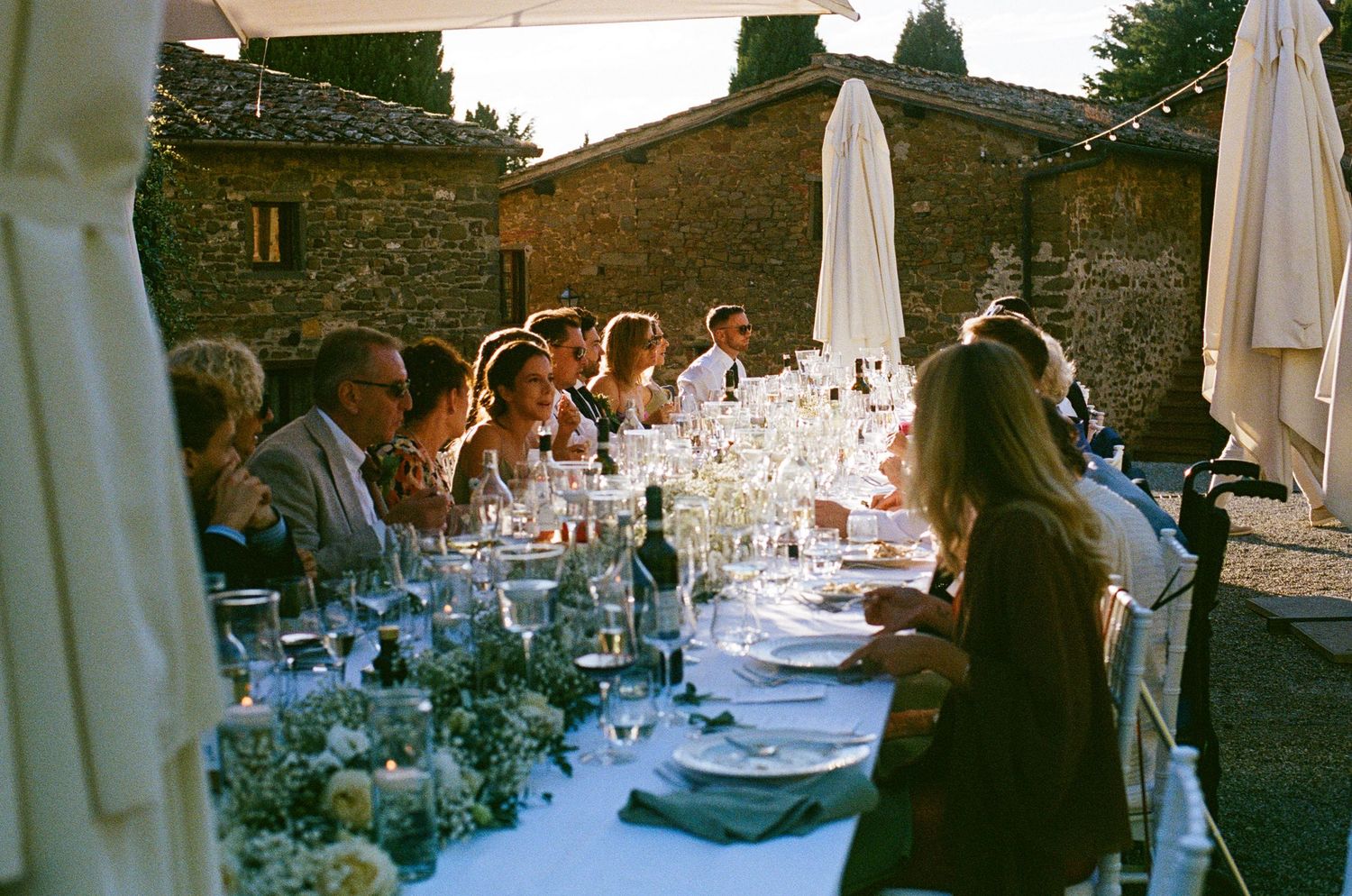Elegant outdoor wedding dinner with floral centerpieces and candles at a rustic Italian stone villa at dusk.