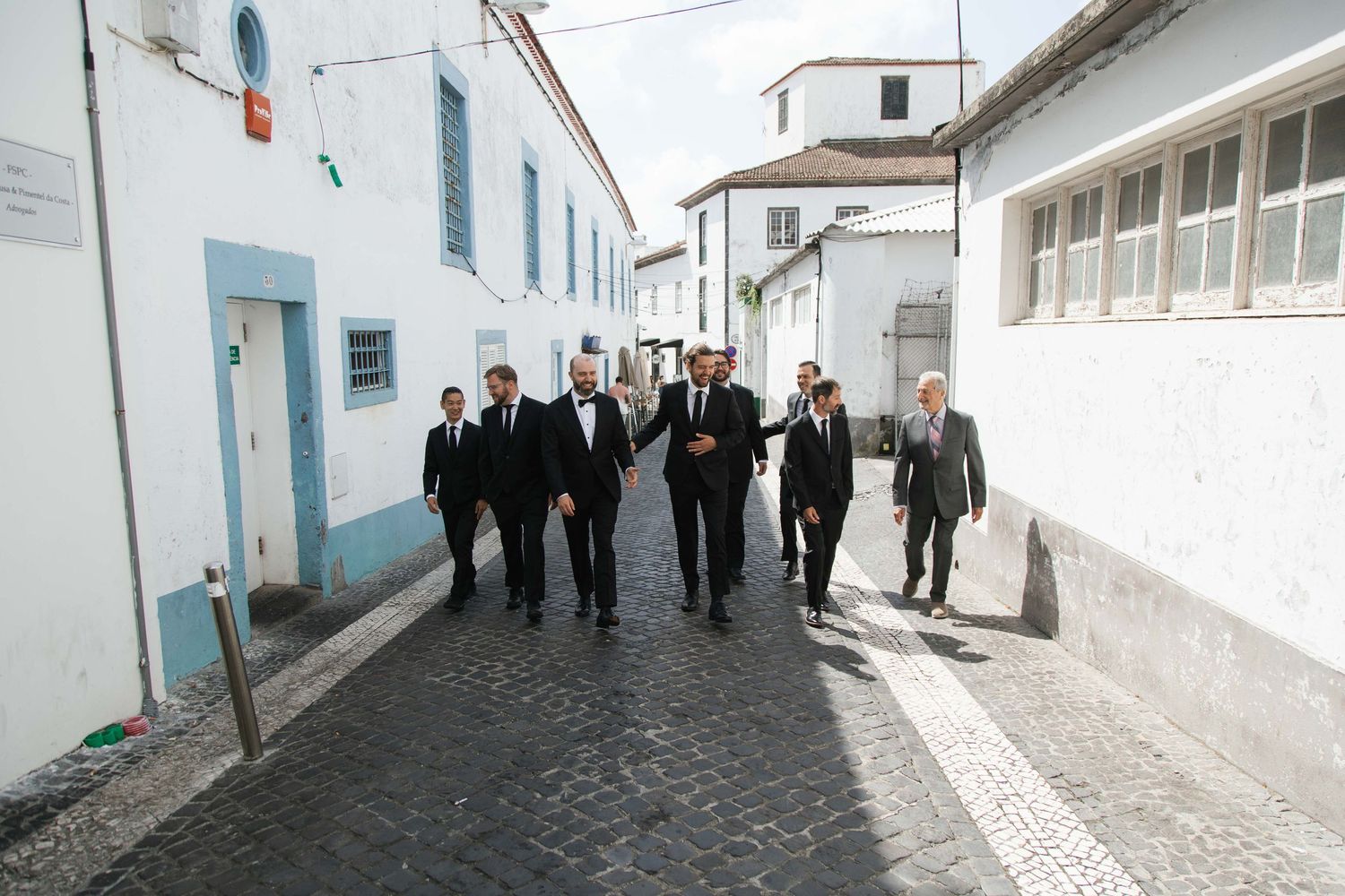 Elegantly dressed wedding guests walking through a charming cobblestone street in Portugal.
