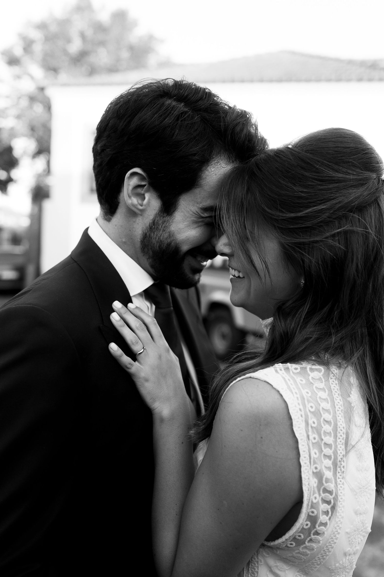 Black and white photo of a couple sharing an intimate moment, touching foreheads and smiling at each other.