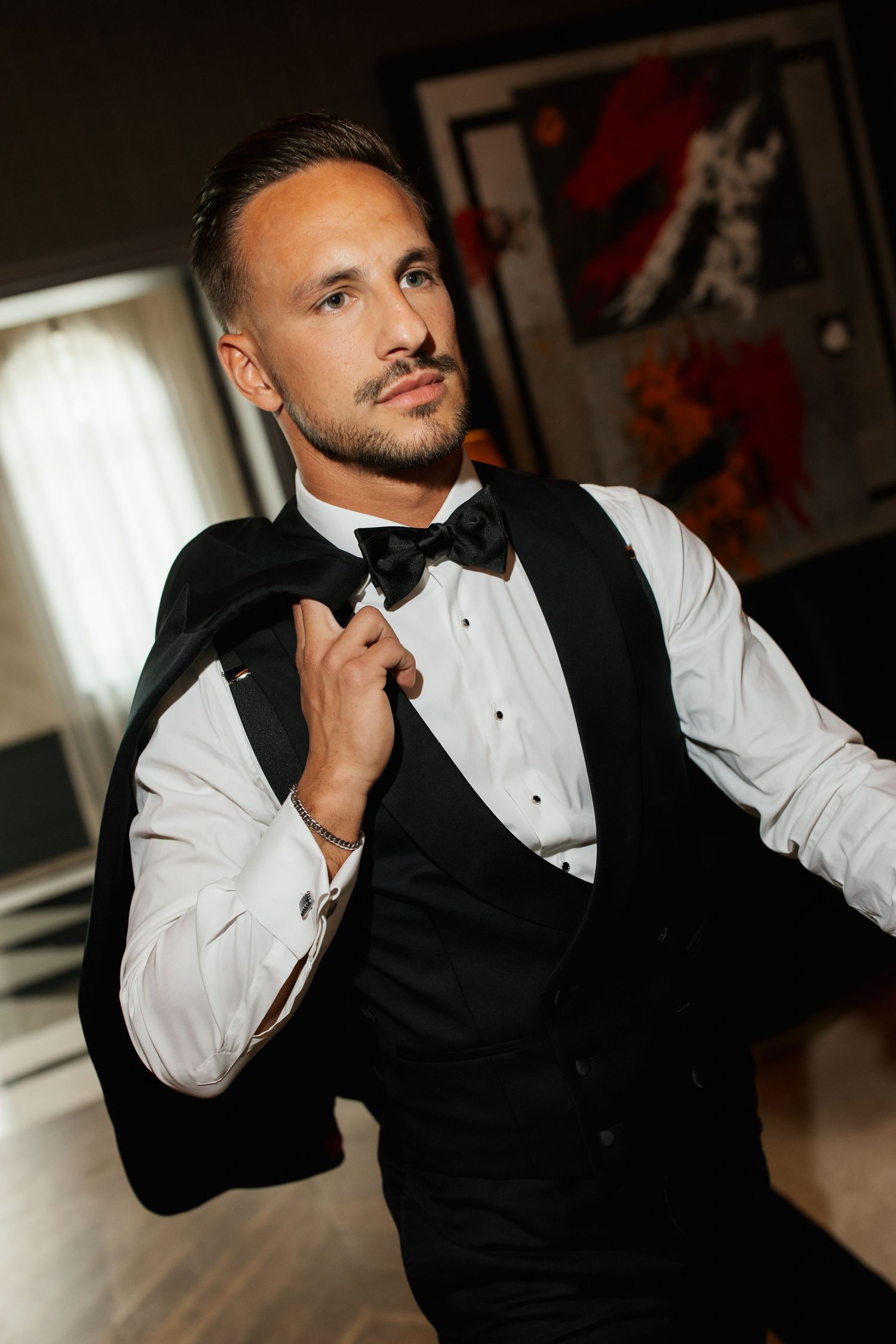 Handsome groom in black tuxedo vest and bow tie preparing for his wedding ceremony indoors.