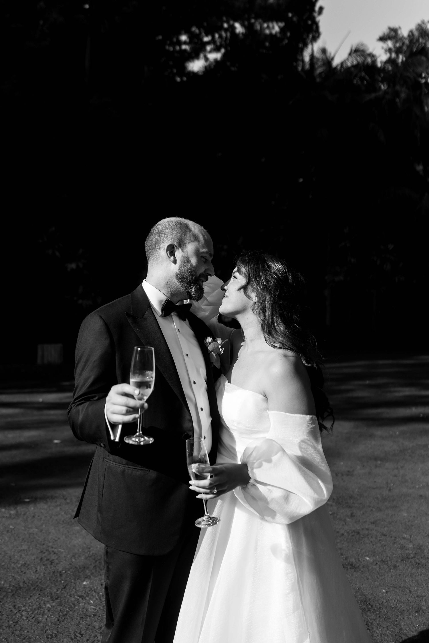 Black and white photo of bride and groom sharing romantic moment while holding champagne flutes.