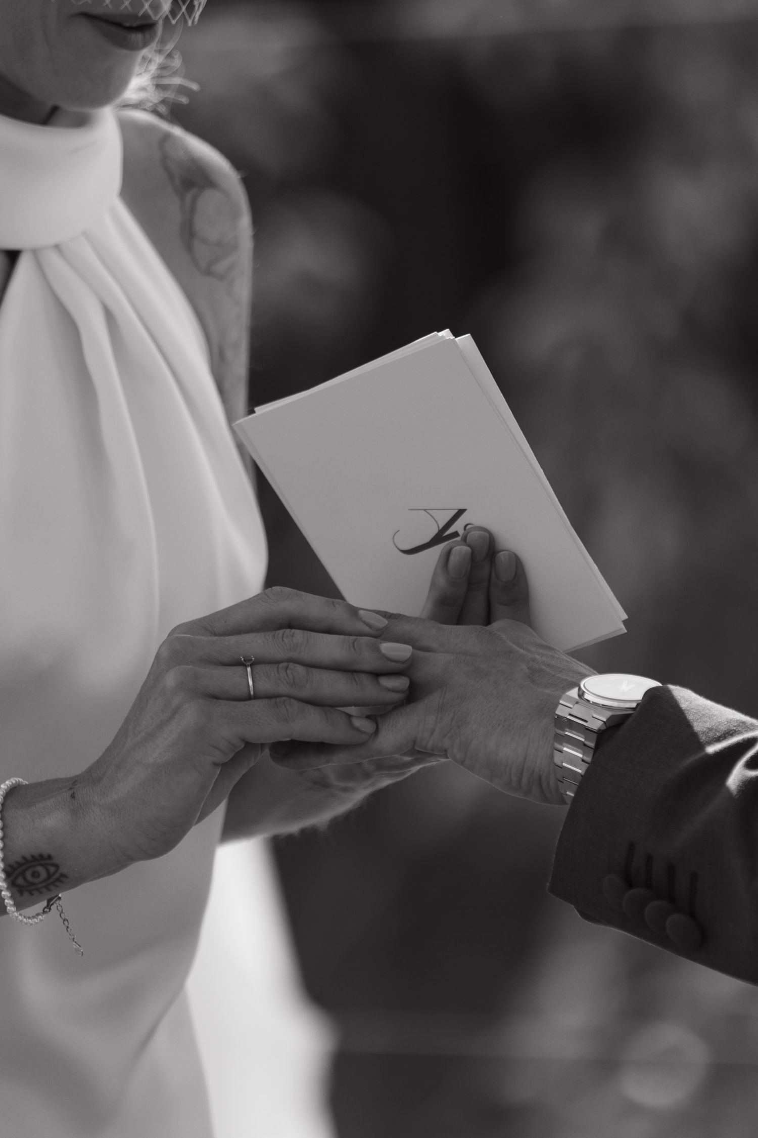 Black and white close-up of bride and groom exchanging rings during outdoor wedding ceremony.